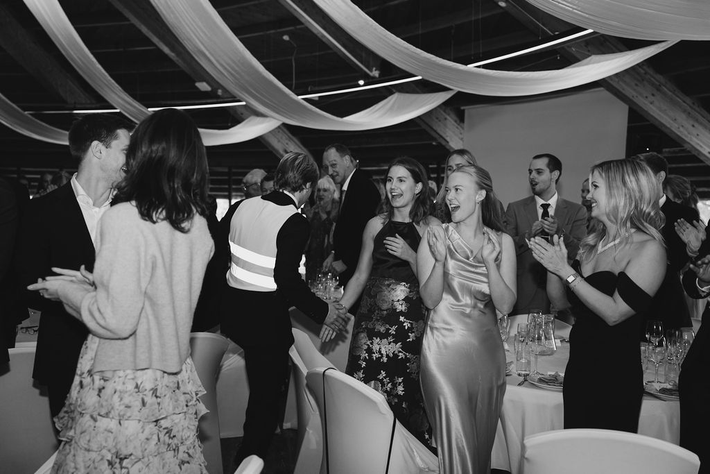 Black and white photo of people dancing and celebrating at an elegant event with draped fabric decor overhead.