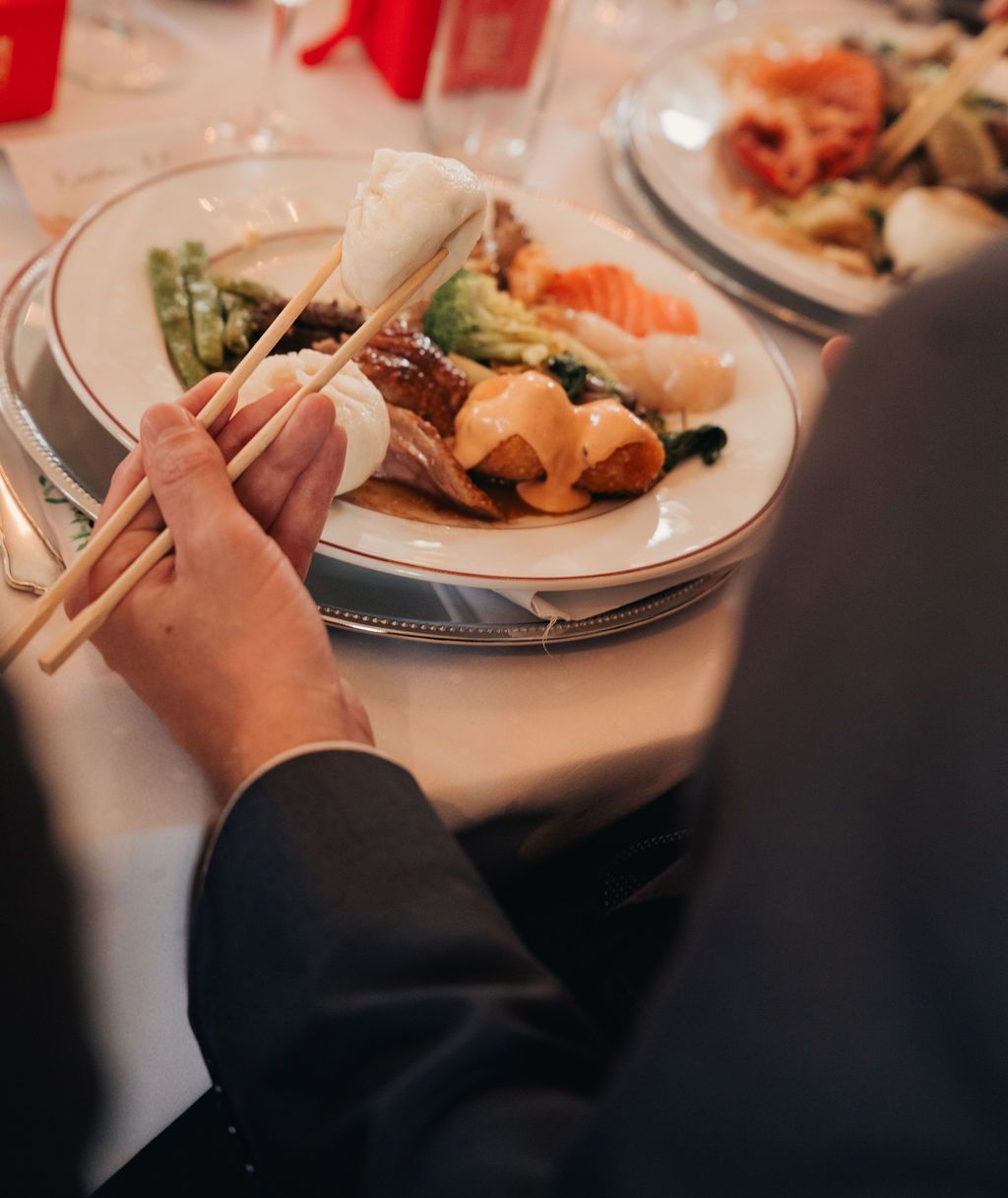 Person using chopsticks to eat sushi and Asian cuisine from elegant white plates on a tablecloth.