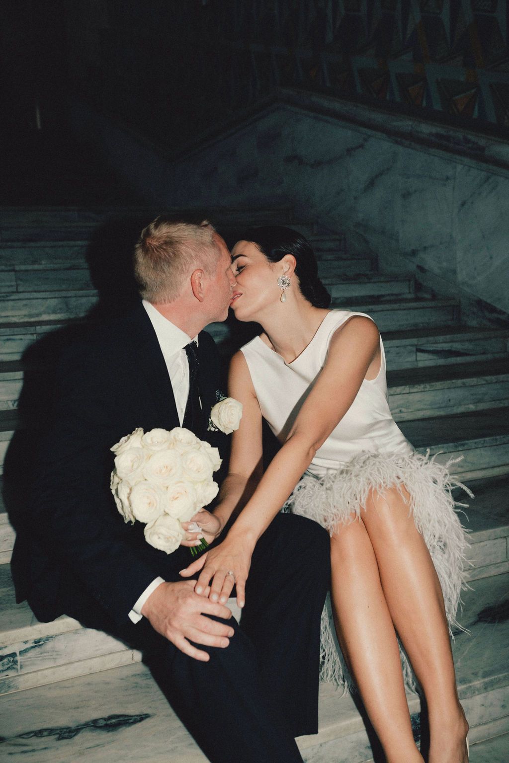 Romantic black and white photo of newlyweds sharing intimate moment in vintage car with white bouquet.
