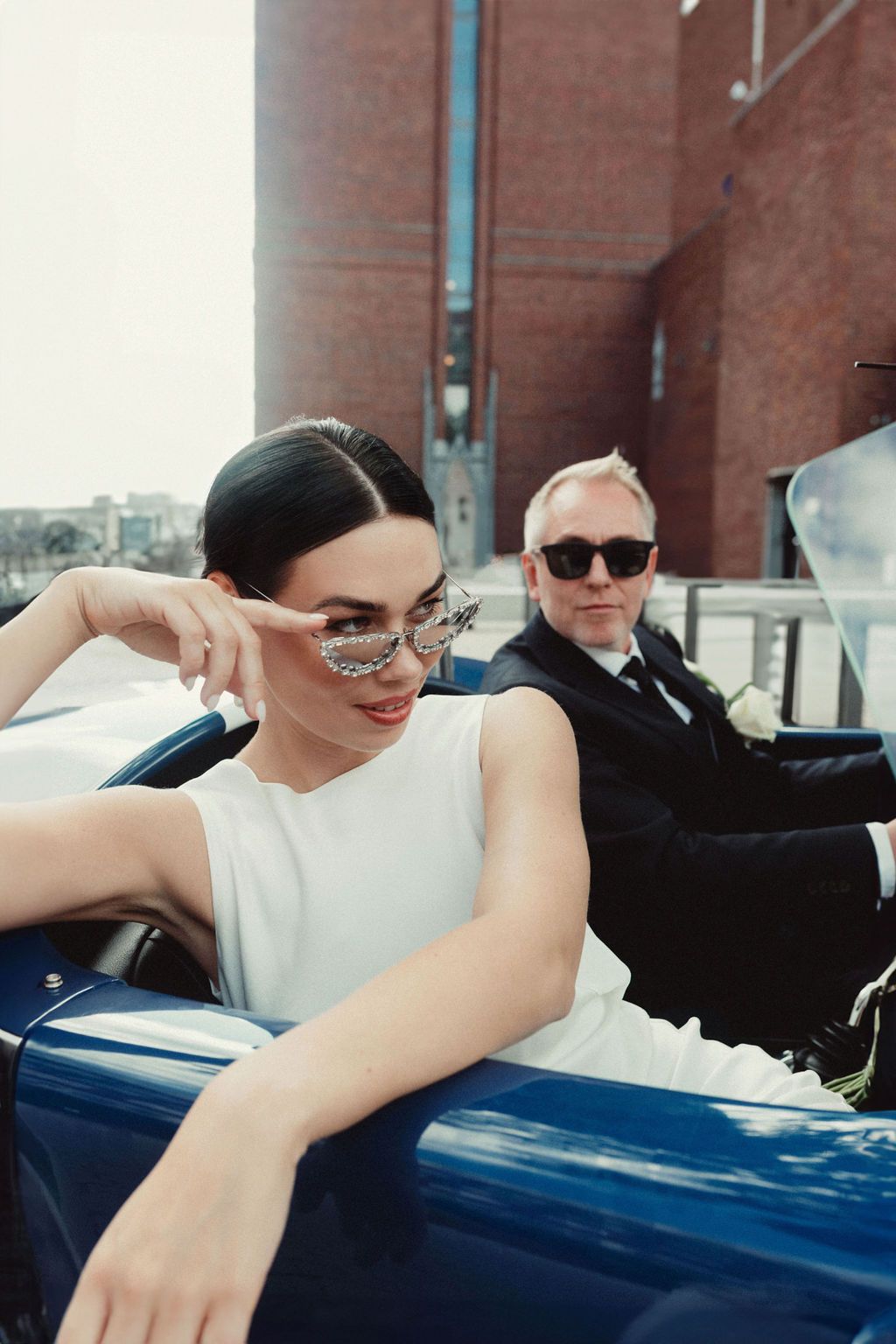 A couple poses casually against a blue car in a series of candid shots with a brick building in the background.
