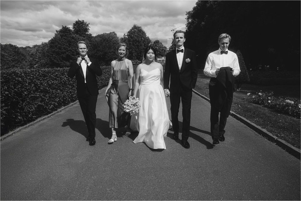 A black and white panoramic sequence showing a wedding party walking along a path outdoors.