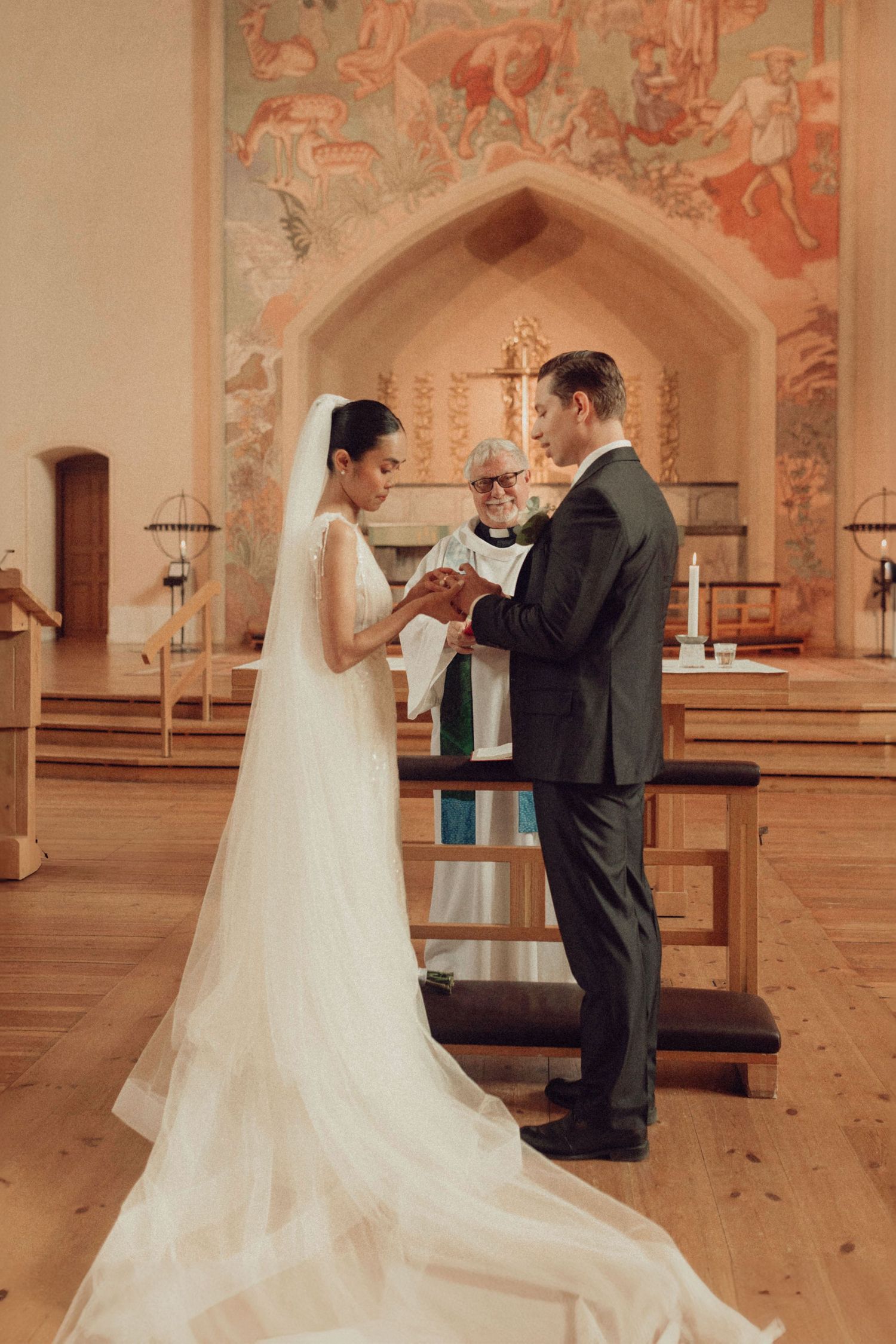 A wedding ceremony takes place in an elegant church with peach-colored frescoed walls and arched architecture.