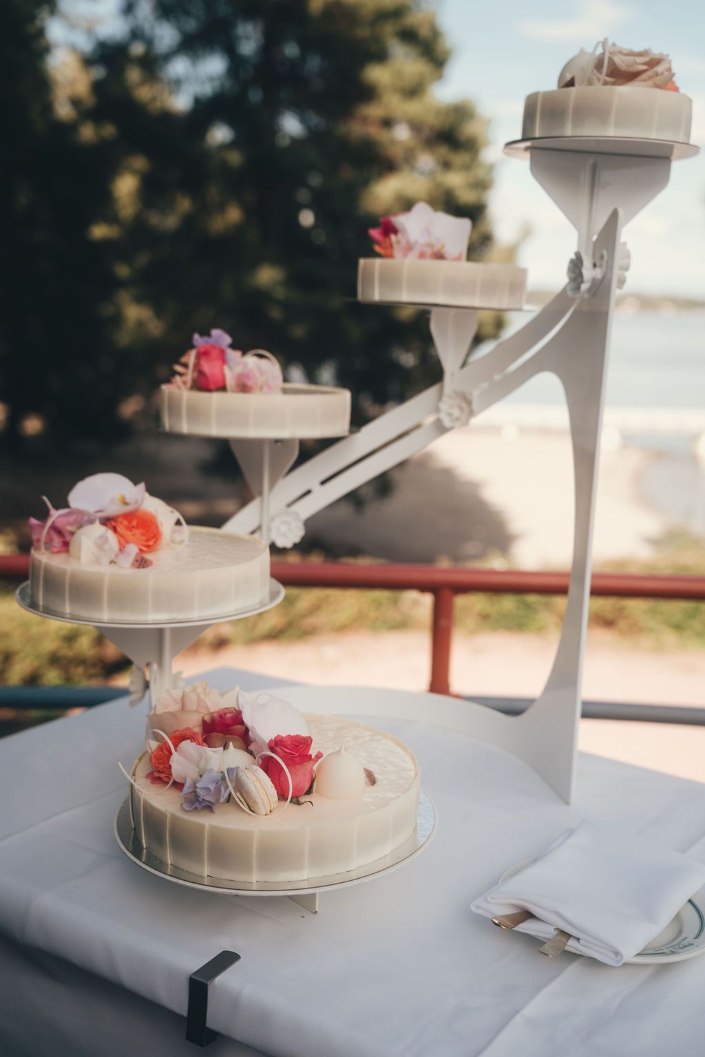 Multi-tiered white wedding cake stand decorated with delicate flowers and ribbons displayed on a white tablecloth.