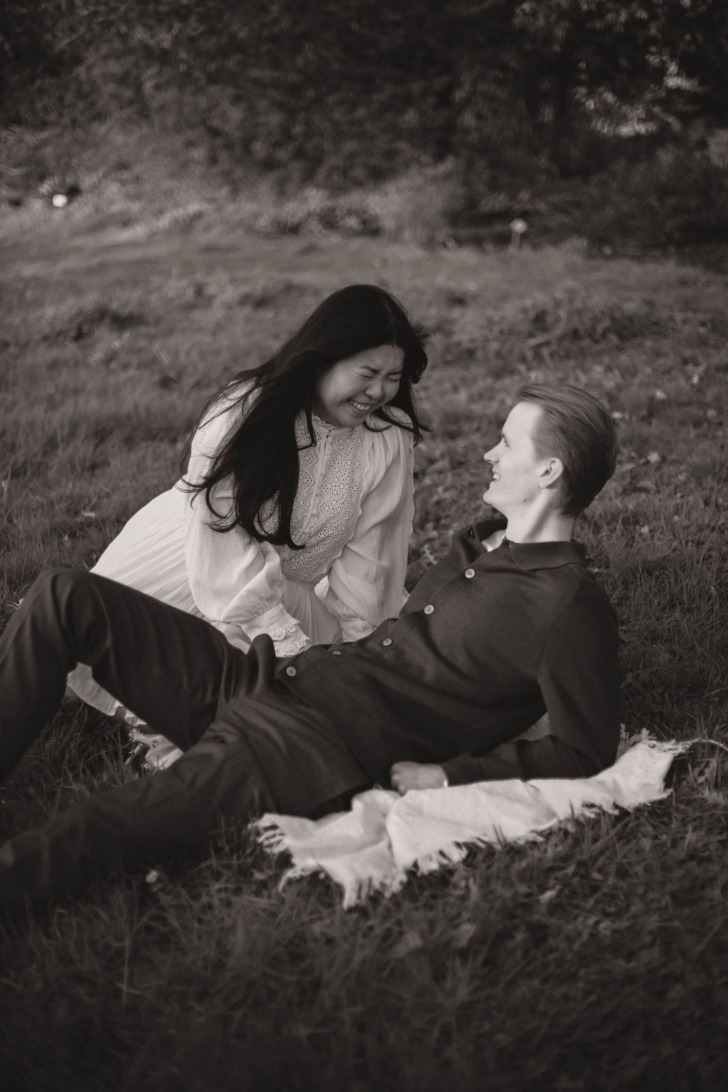 A couple lying together in tall grass outdoors in a romantic black and white photograph.