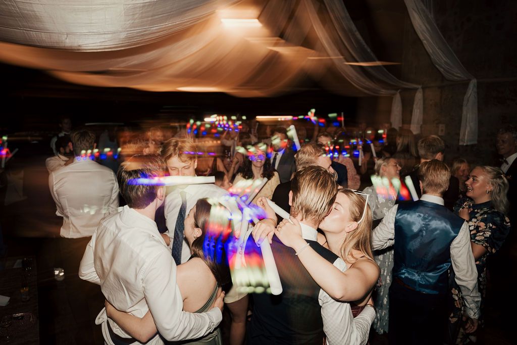 A group of people dancing together at a wedding reception with colorful lighting and a festive atmosphere.