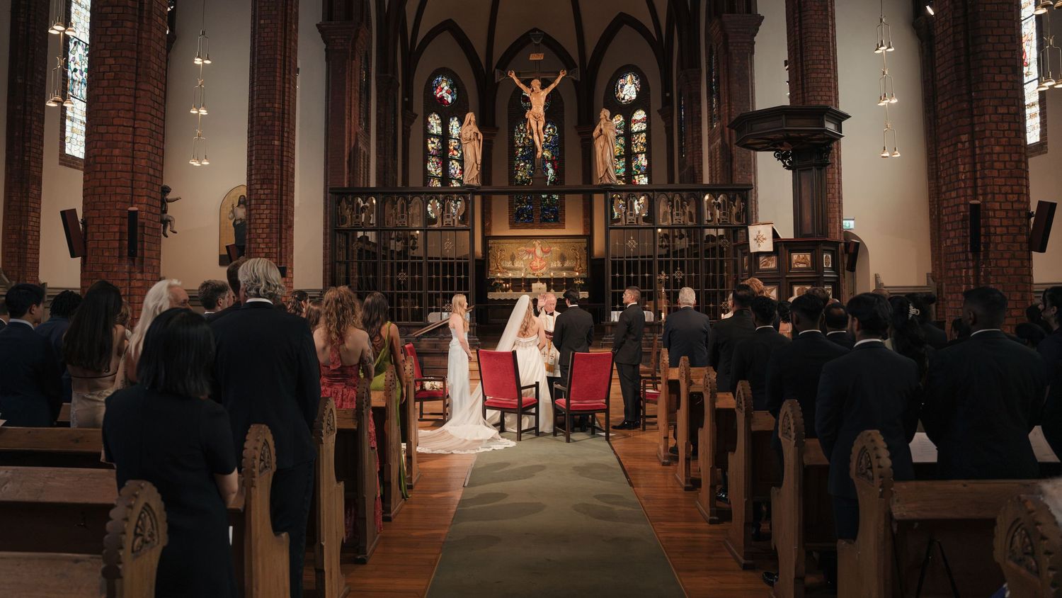 Bride and groom stand at the altar of a historic church during a wedding ceremony as guests watch from the wooden pews.
