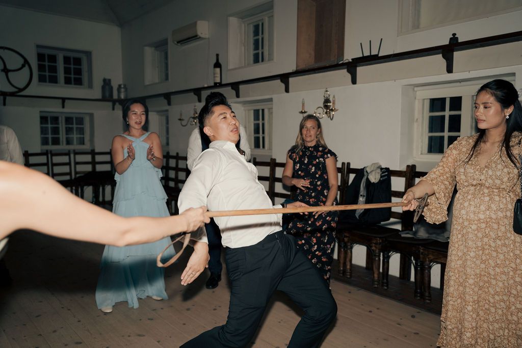 People dancing and socializing in a large room with windows and wooden floors.