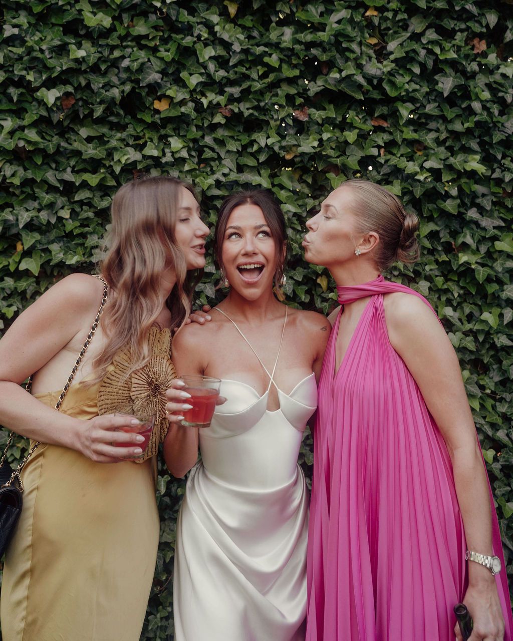 A group of bridesmaids in pink and yellow dresses share laughter and hugs during a wedding celebration.