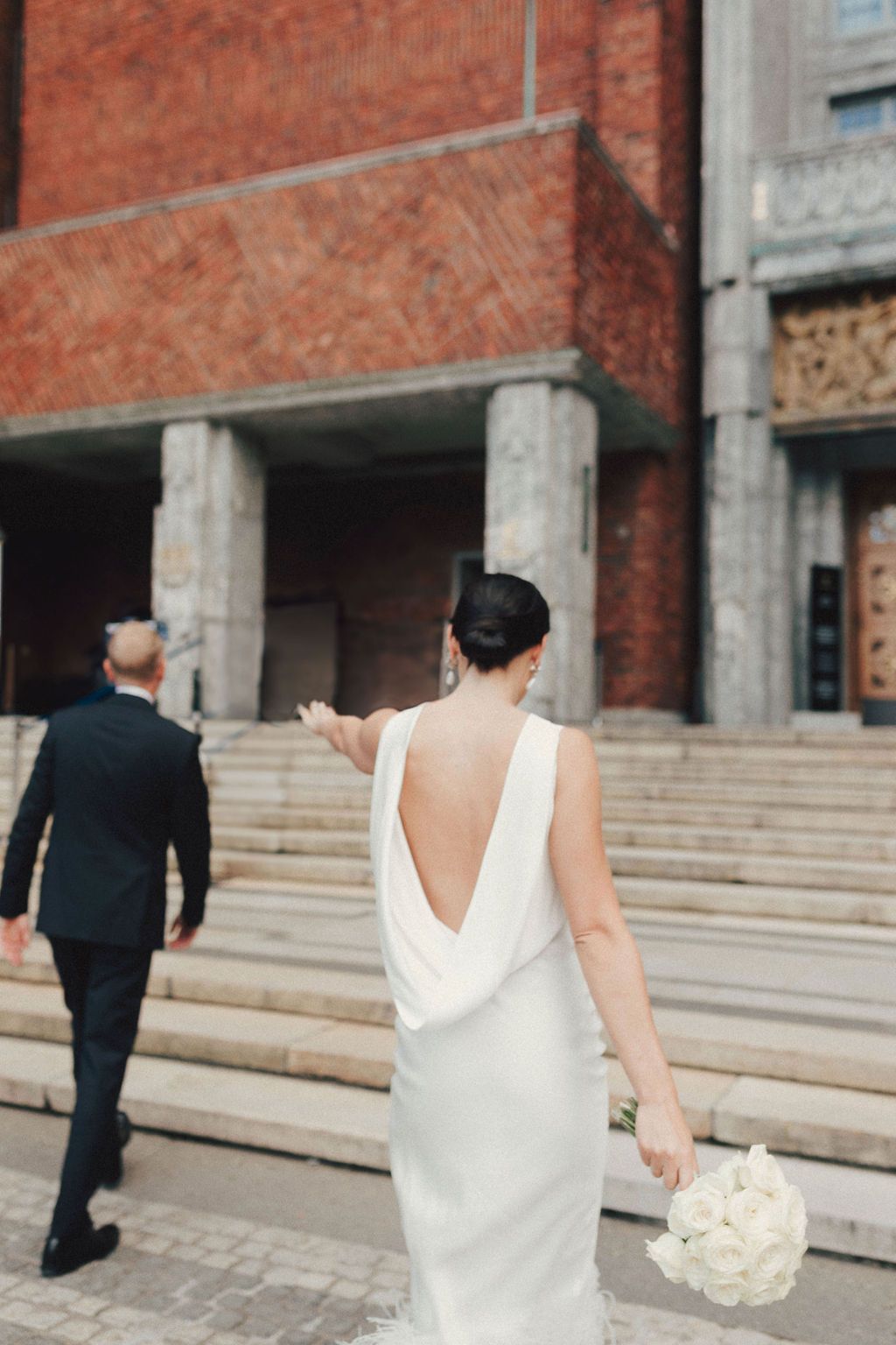 A bride in a white dress walks past stone columns and brick walls during a wedding photoshoot.