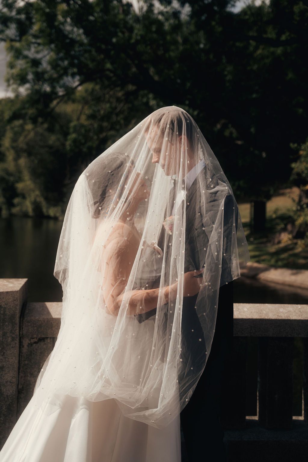 A delicate white wedding veil flows gracefully in the sunlight against a lake backdrop.