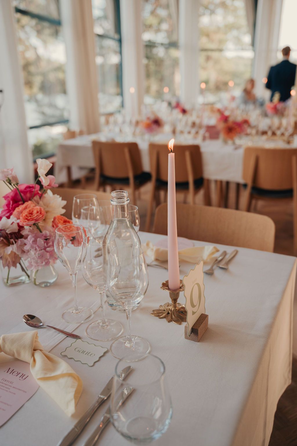 Elegant wedding reception table setting with white linens, wine glasses, and soft pink floral centerpieces.