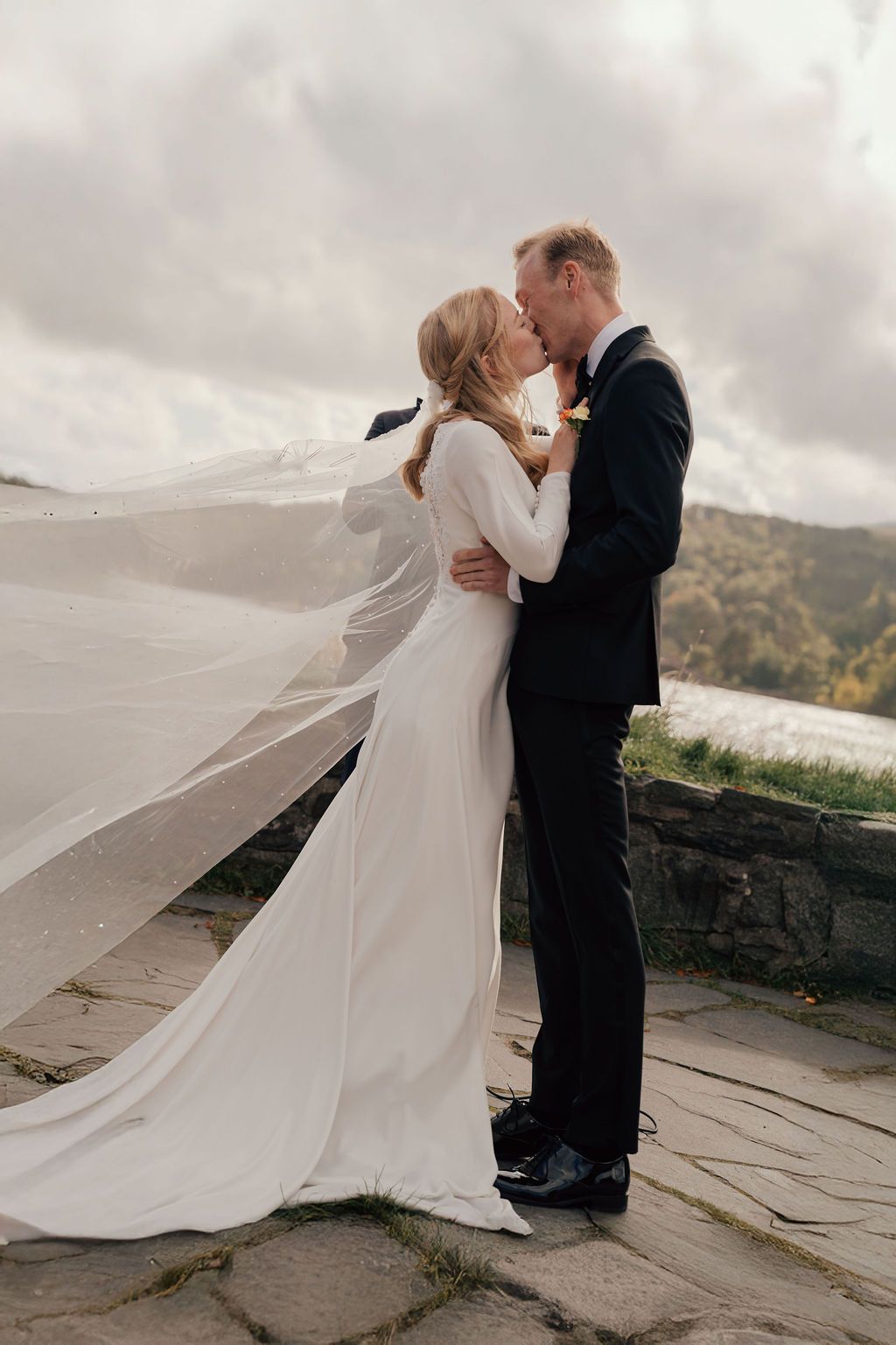 A romantic wedding moment captured on a mountaintop with a flowing white dress veil caught in the wind.