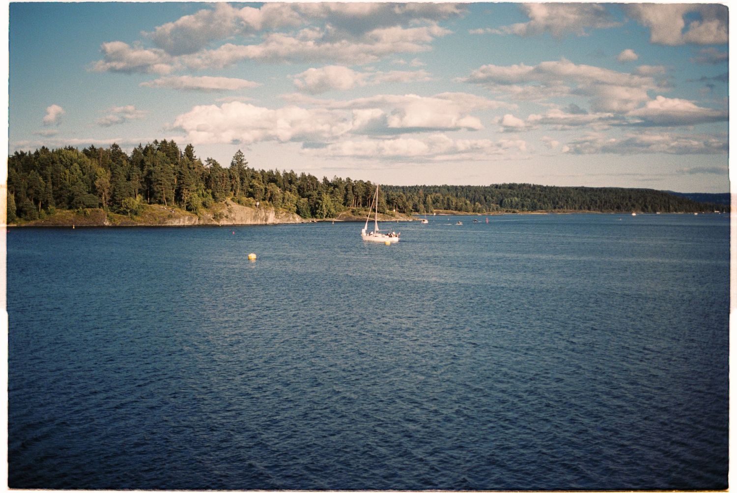 Scenic Swedish archipelago with a sailboat on calm blue waters surrounded by forested islands.