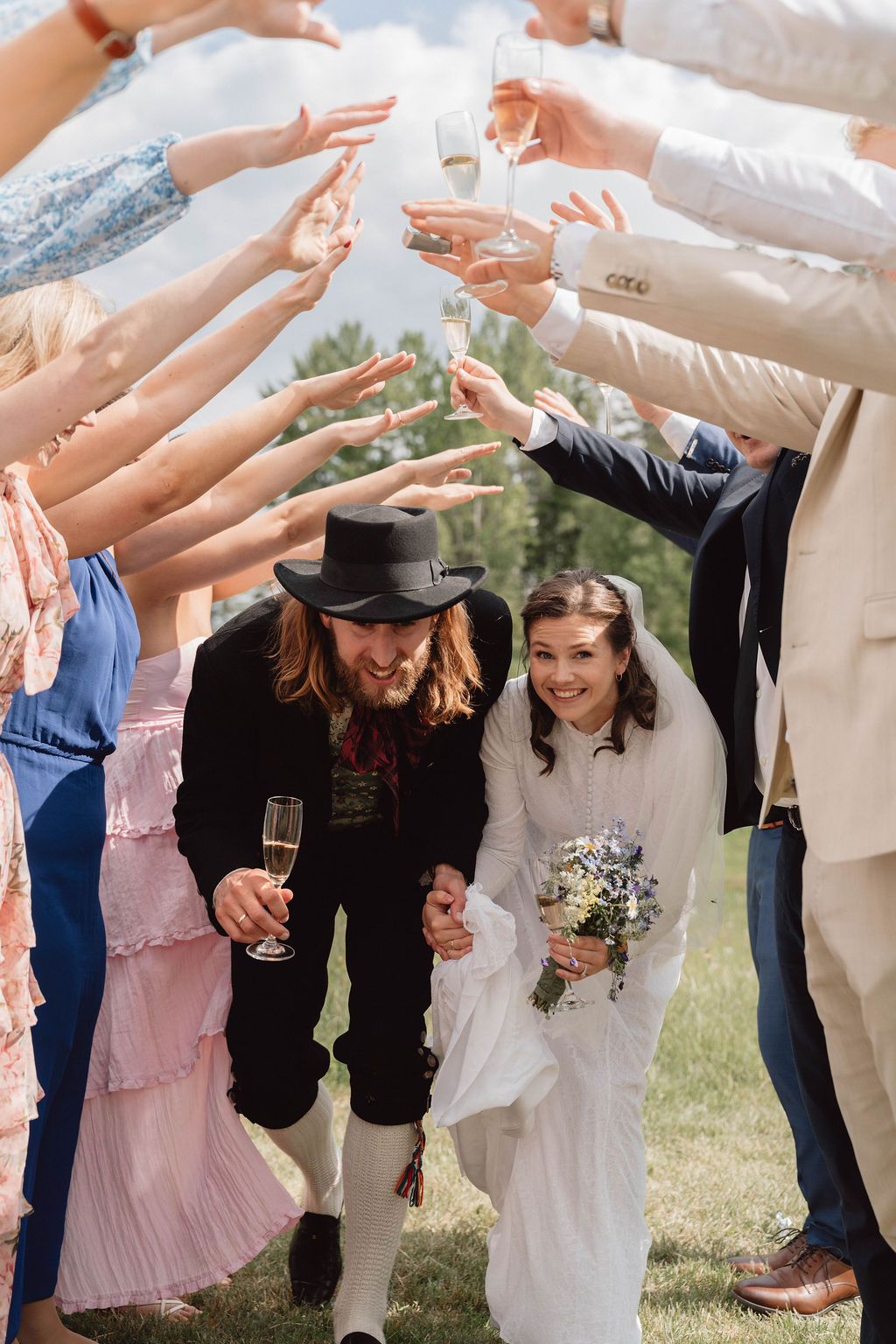 Wedding party creates a tunnel with raised arms as the newlyweds walk through during outdoor celebration.