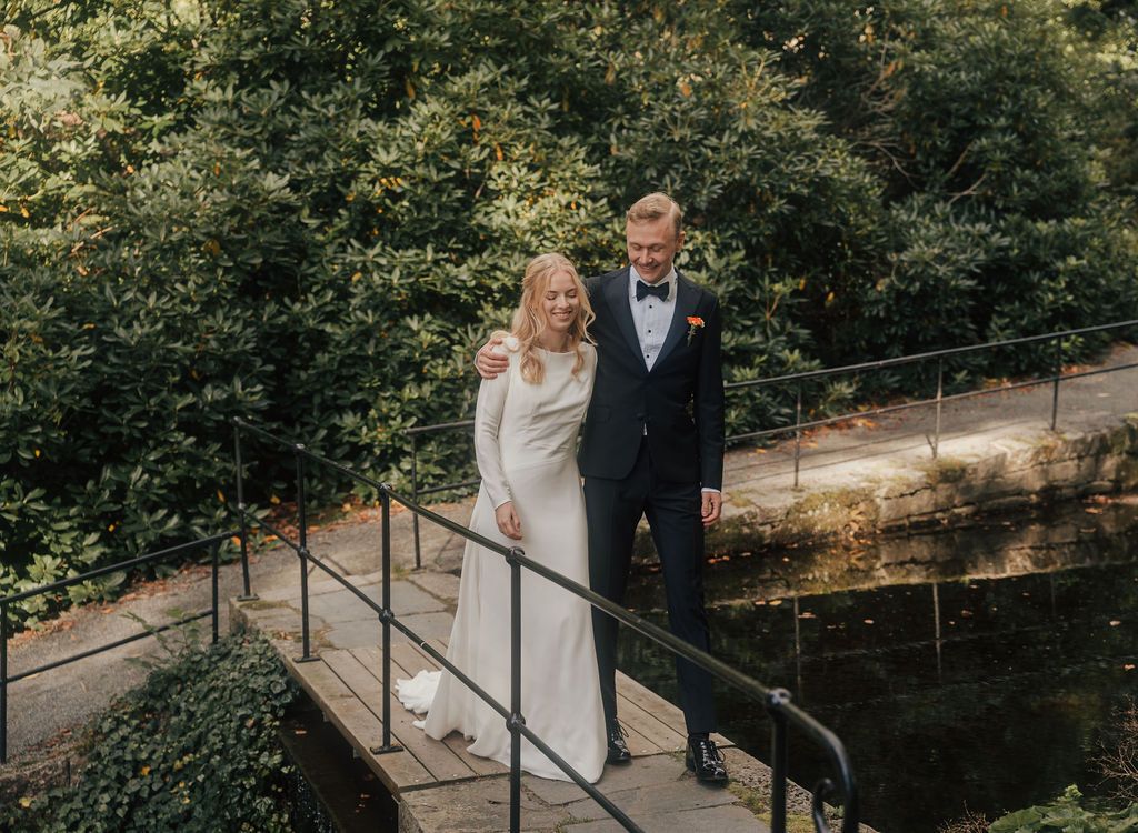A couple poses together on a rustic bridge surrounded by lush greenery on their wedding day.