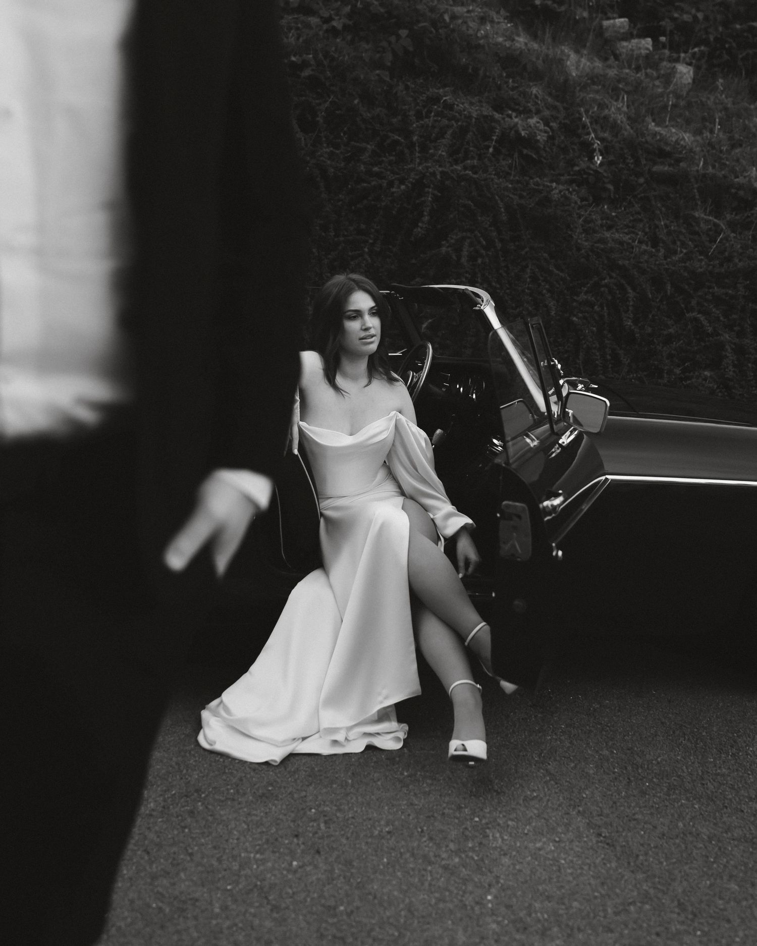 Black and white artistic photograph of someone in a white dress sitting on grass in a contemplative pose.