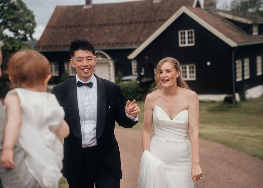 Wedding party walking and laughing together on a path near rustic buildings.