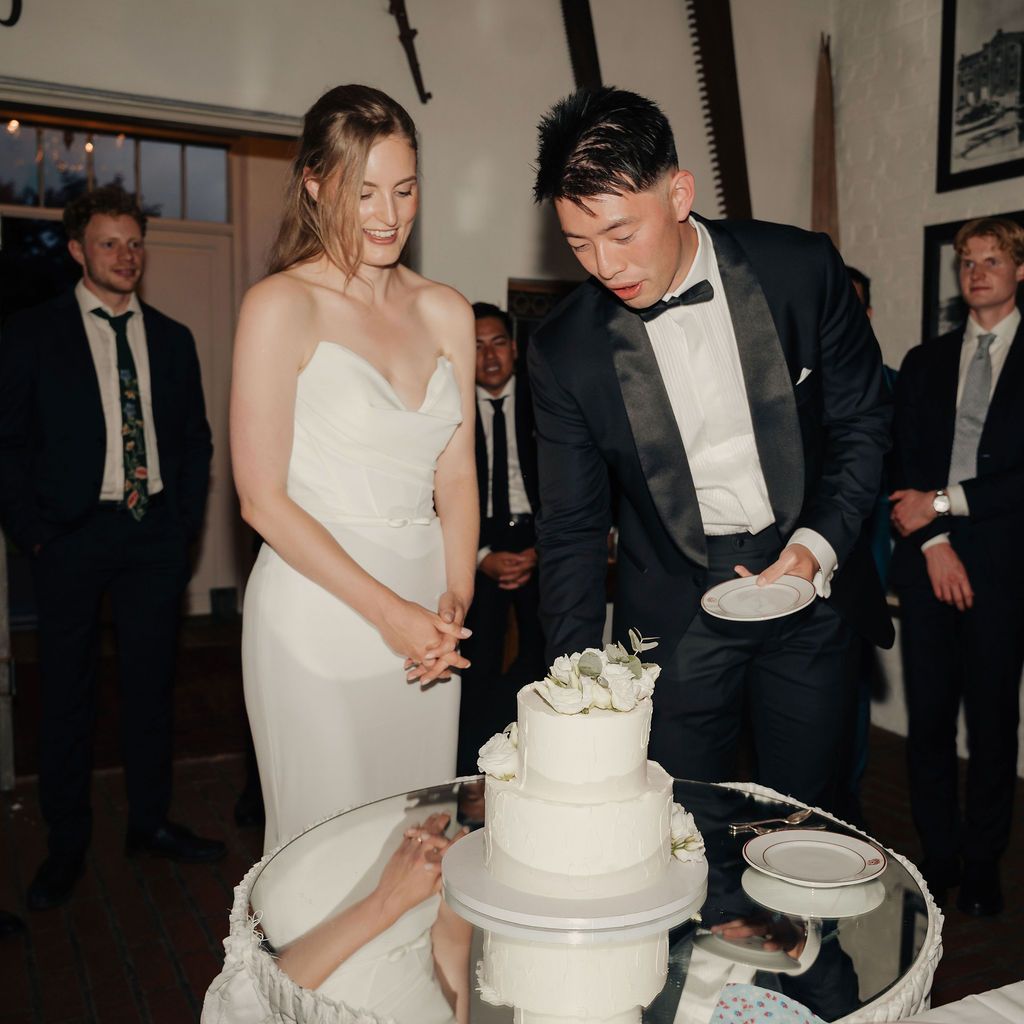A couple cutting their wedding cake together in a traditional cake-cutting ceremony at their reception.