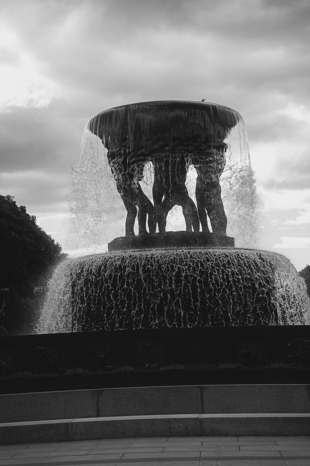 A black and white panoramic sequence showing a dramatic fountain silhouette against a moody clouded sky.