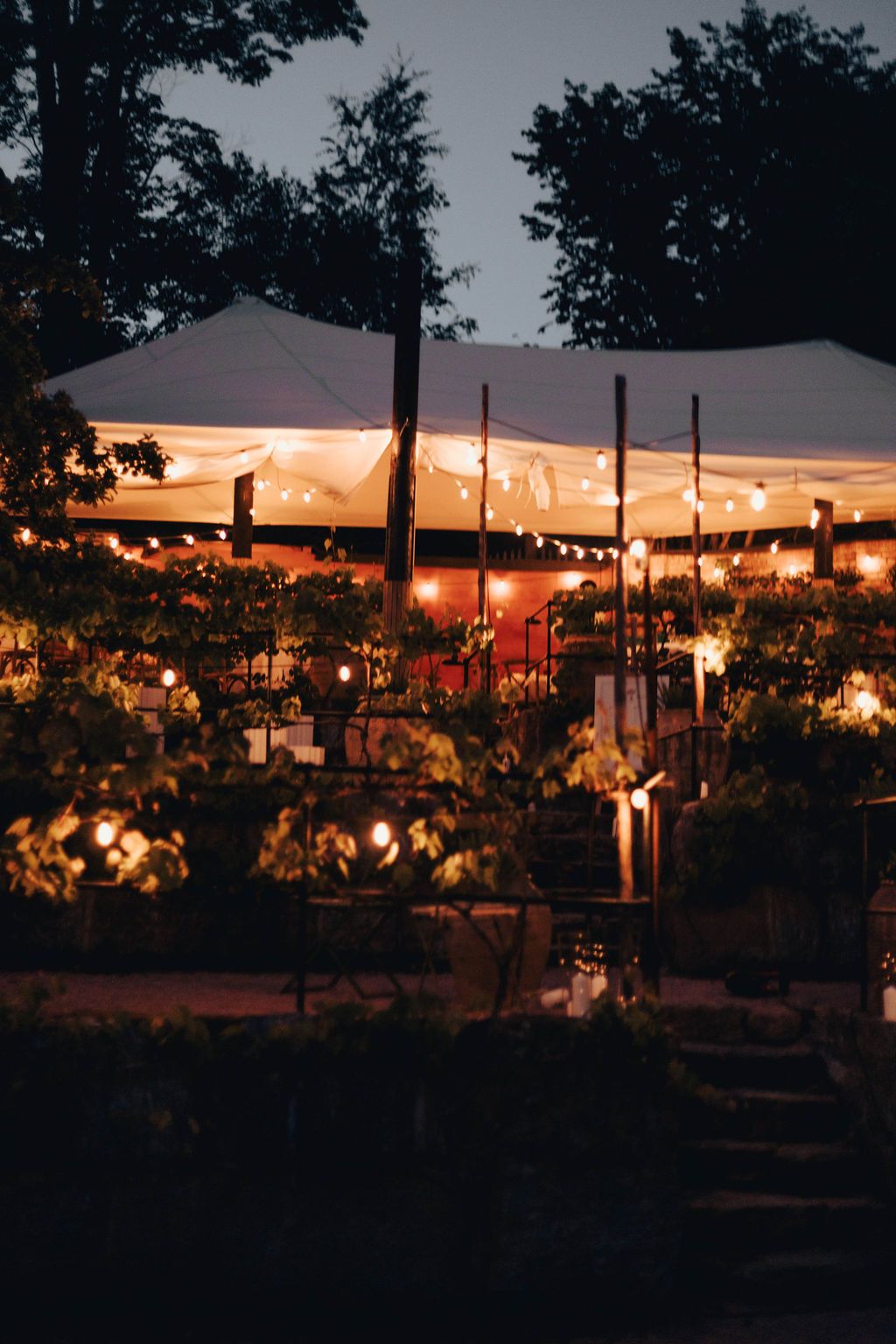 White outdoor tent pavilion illuminated with string lights at sunset creates a romantic ambiance for an evening event.