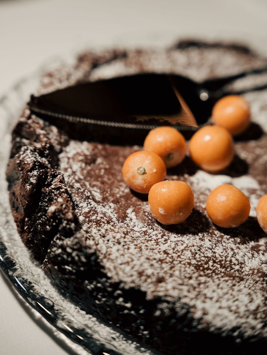 Dark chocolate dessert garnished with orange berries and powdered sugar on a black plate.