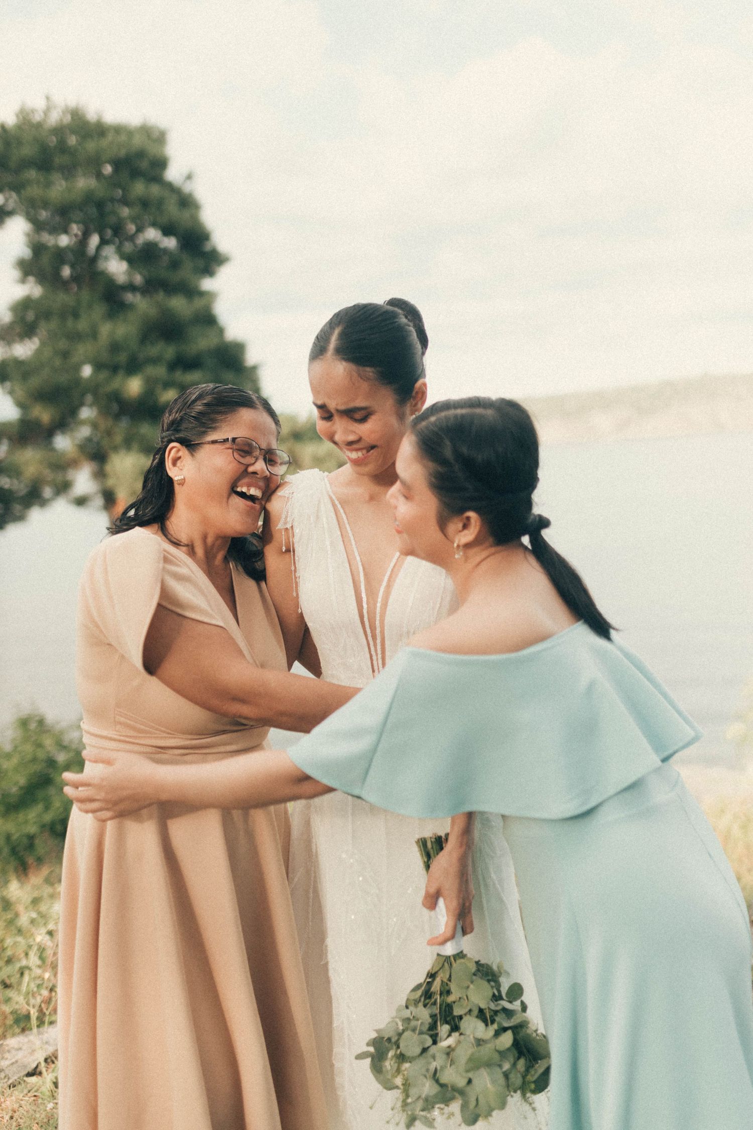 Two women in beige and mint dresses share emotional moments together in an outdoor setting.