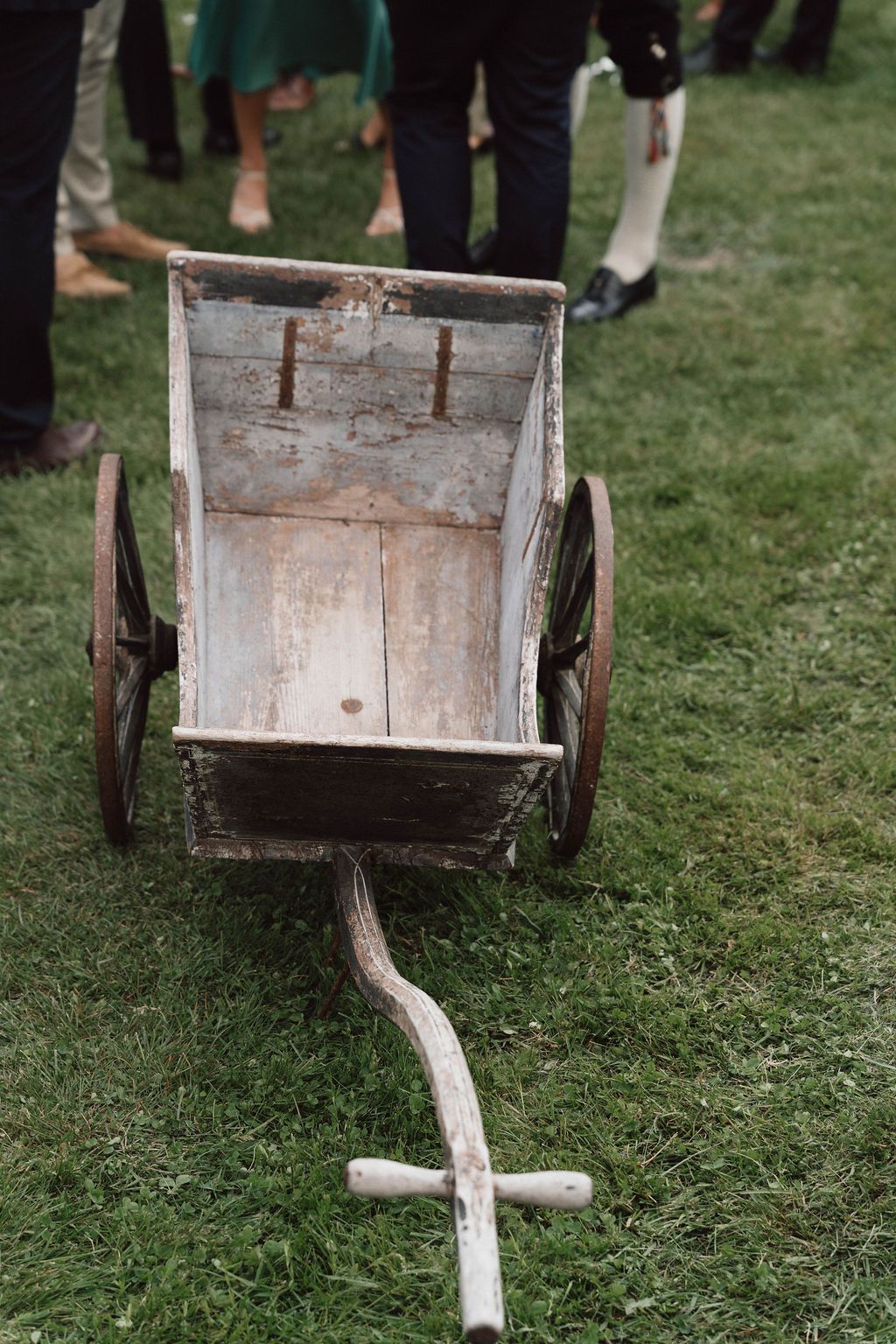 Rustic wooden cart with metal wheels sits on green grass at an outdoor event.