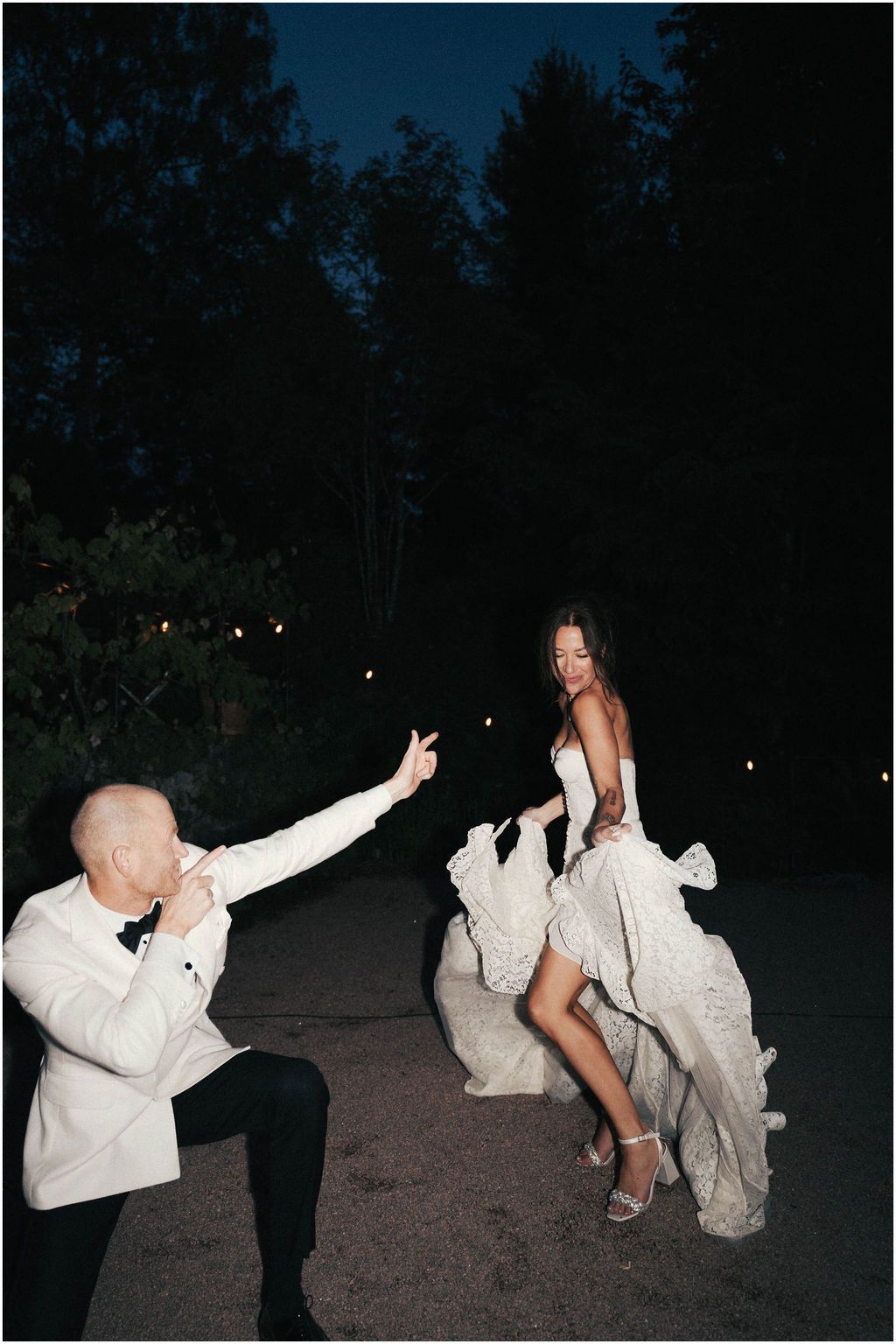 A candid nighttime wedding photo showing a couple dancing and celebrating on a dark outdoor path.