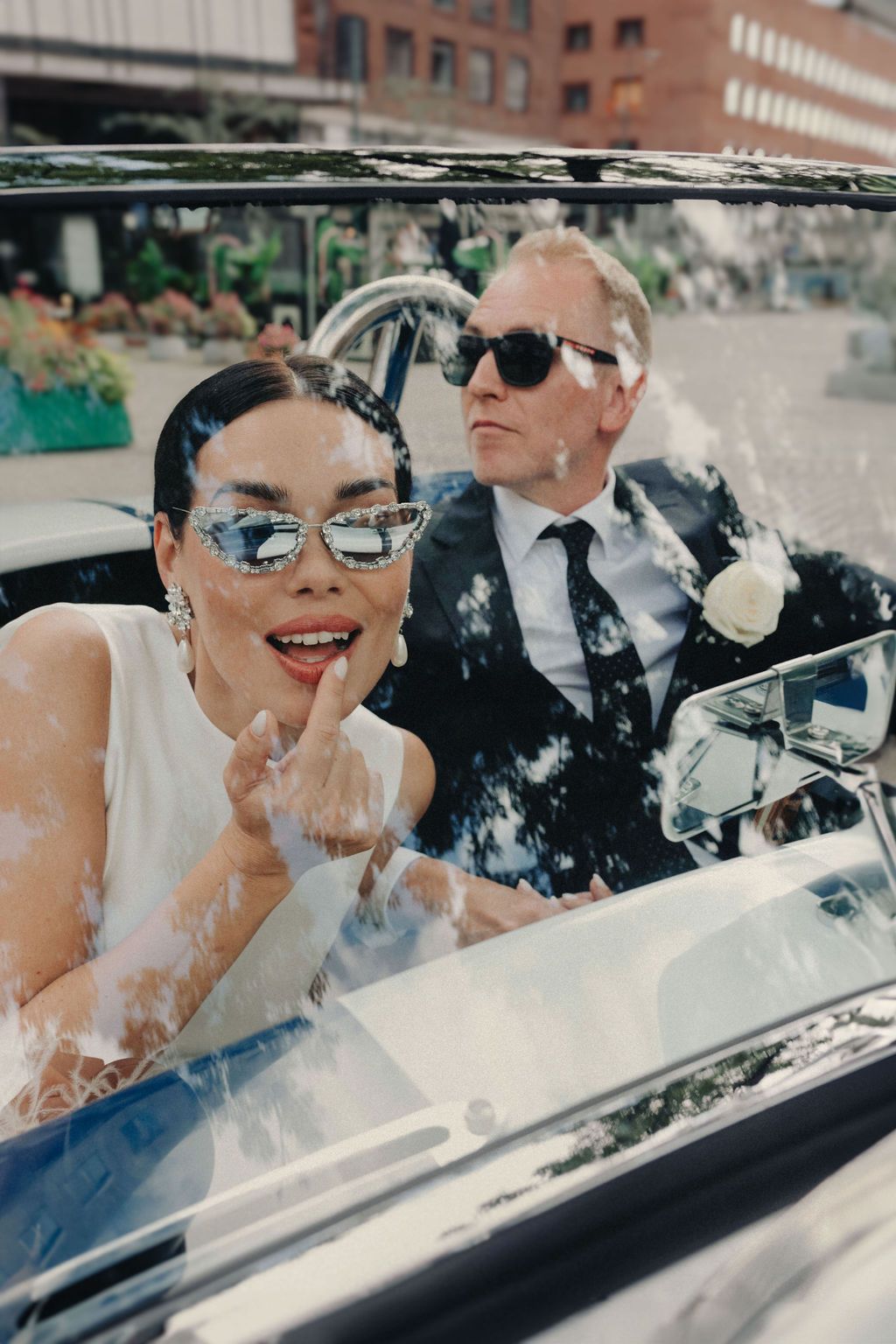 Happy couple laughing together in classic convertible car with sunglasses on sunny day.