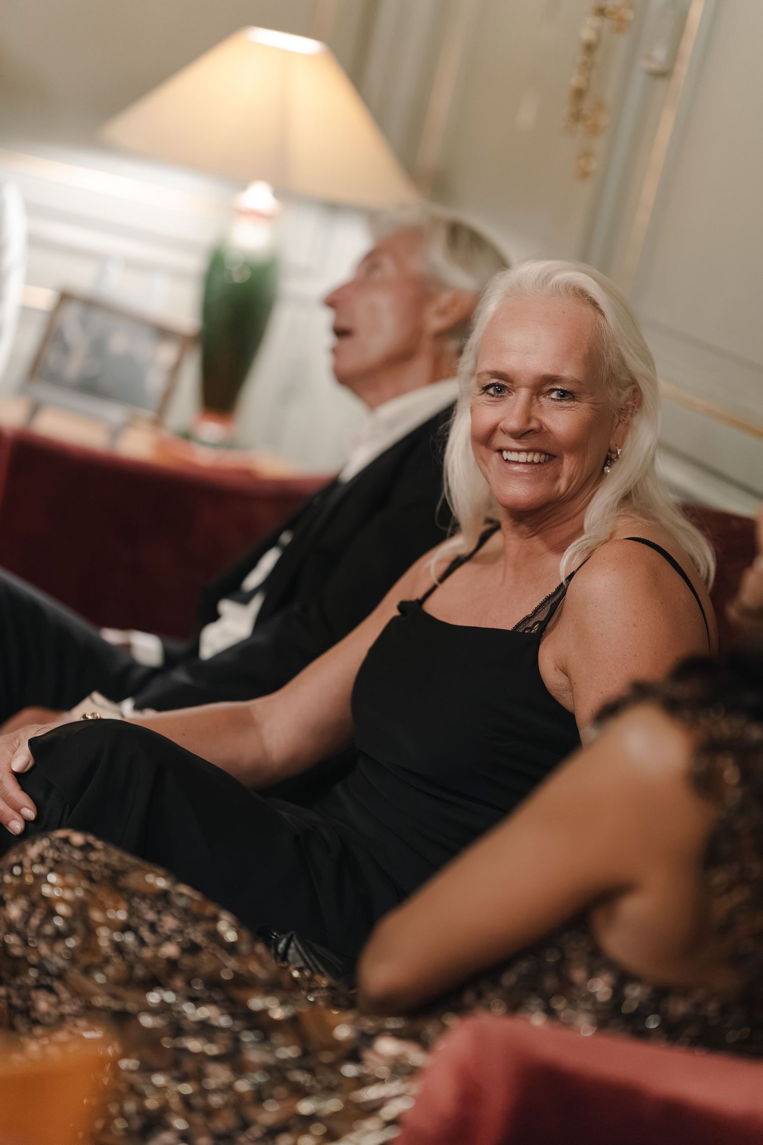Smiling older woman with silver hair in a black dress sits beside a man at an elegant wedding reception.