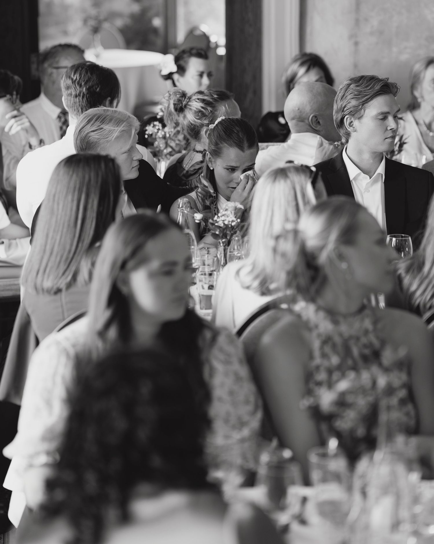Black and white photo of elegantly dressed guests mingling and seated at a formal wedding reception dinner.