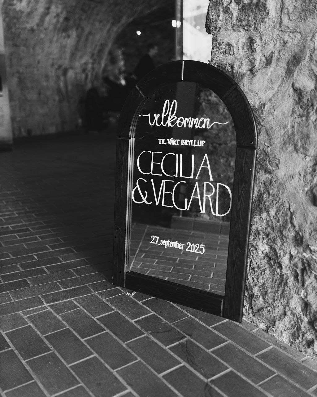 Black and white wedding signage displays names on chalkboards against a rustic stone wall.