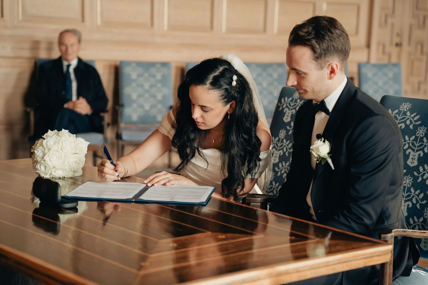 Wedding guests seated at long wooden tables during an elegant reception in a grand ballroom.