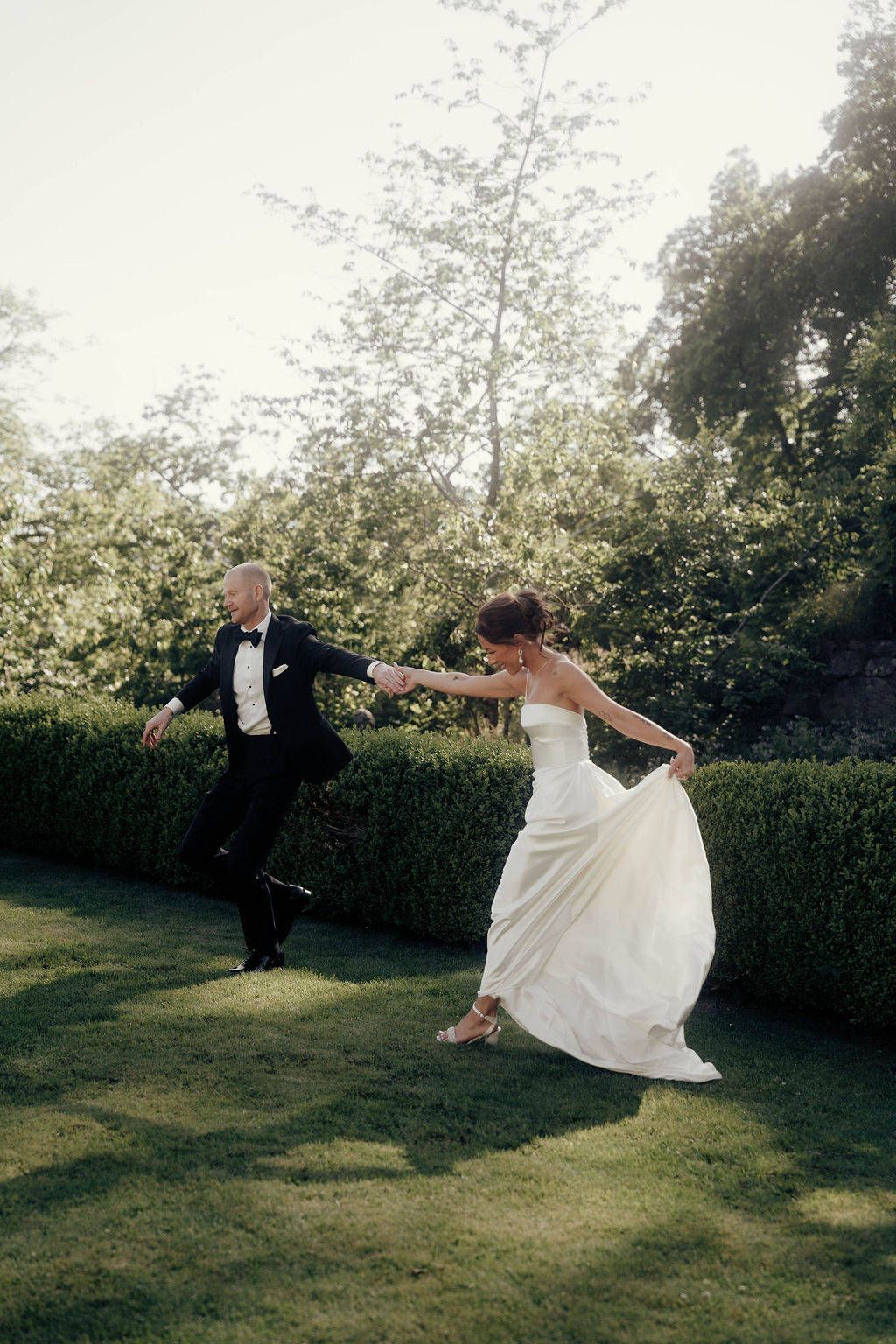 A couple in wedding attire playfully pose in a garden setting, creating a whimsical series of dance-like movements.