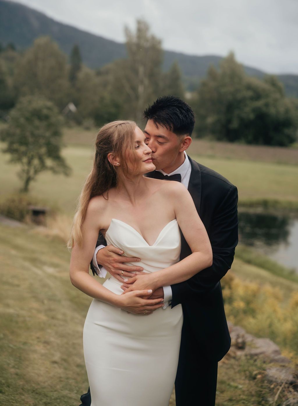 Romantic wedding couple embraces in a scenic mountain landscape with rolling hills and autumn foliage.