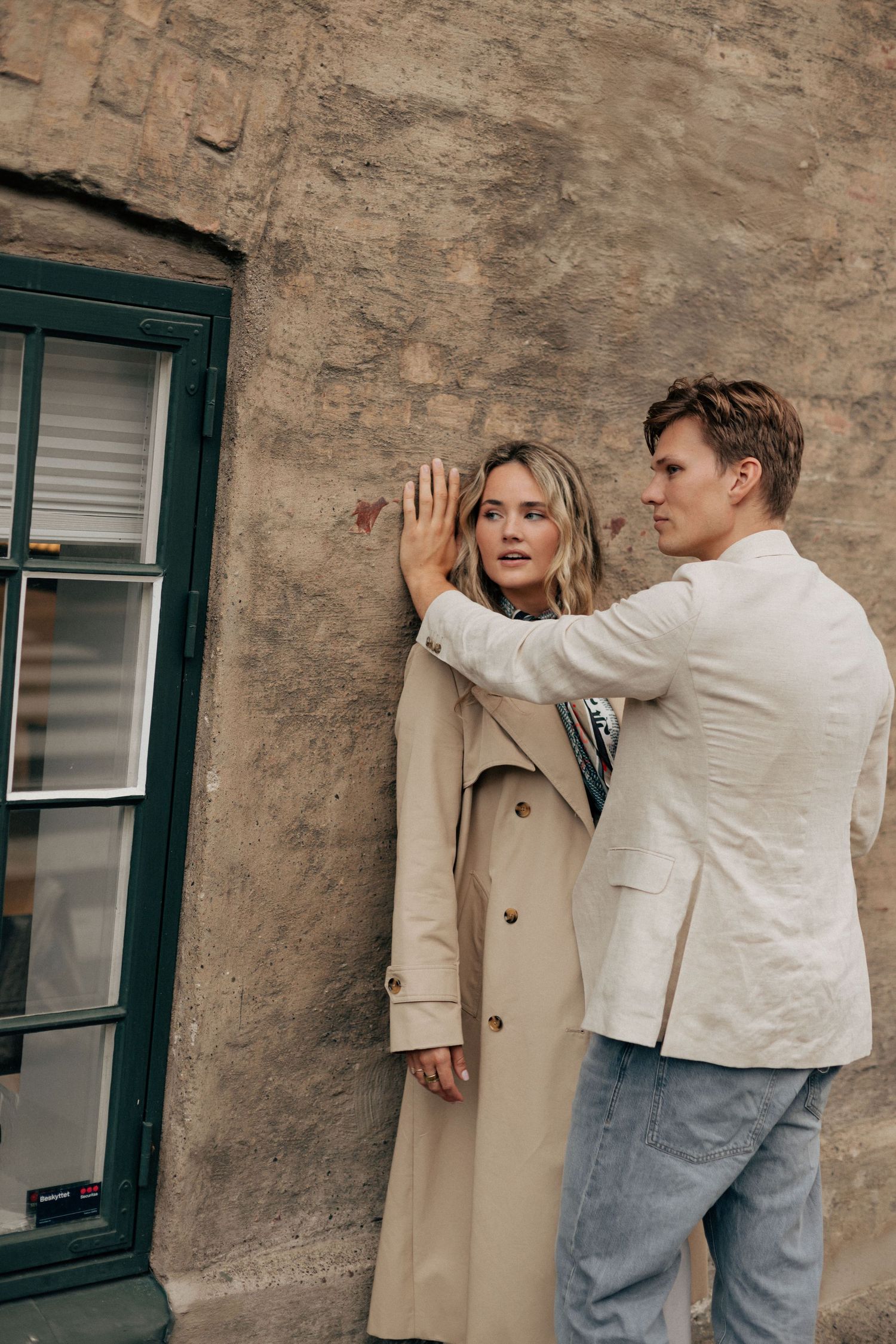 Four sequential photos showing someone in a white jacket reaching up to touch a beige coat hanging on a stone wall.