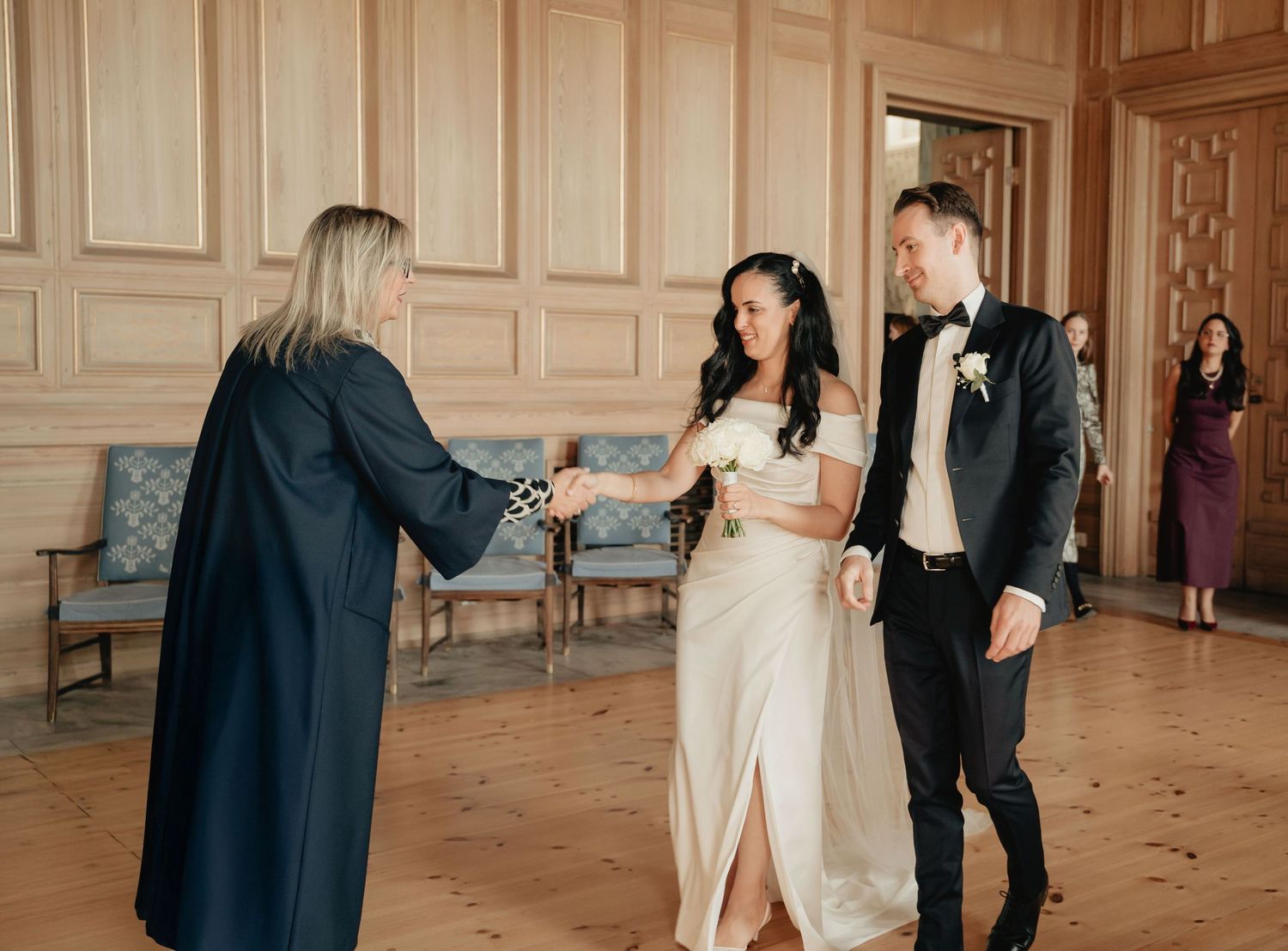 A couple in formal attire dance together in an elegant ballroom with ornate wall panels and wooden floors.