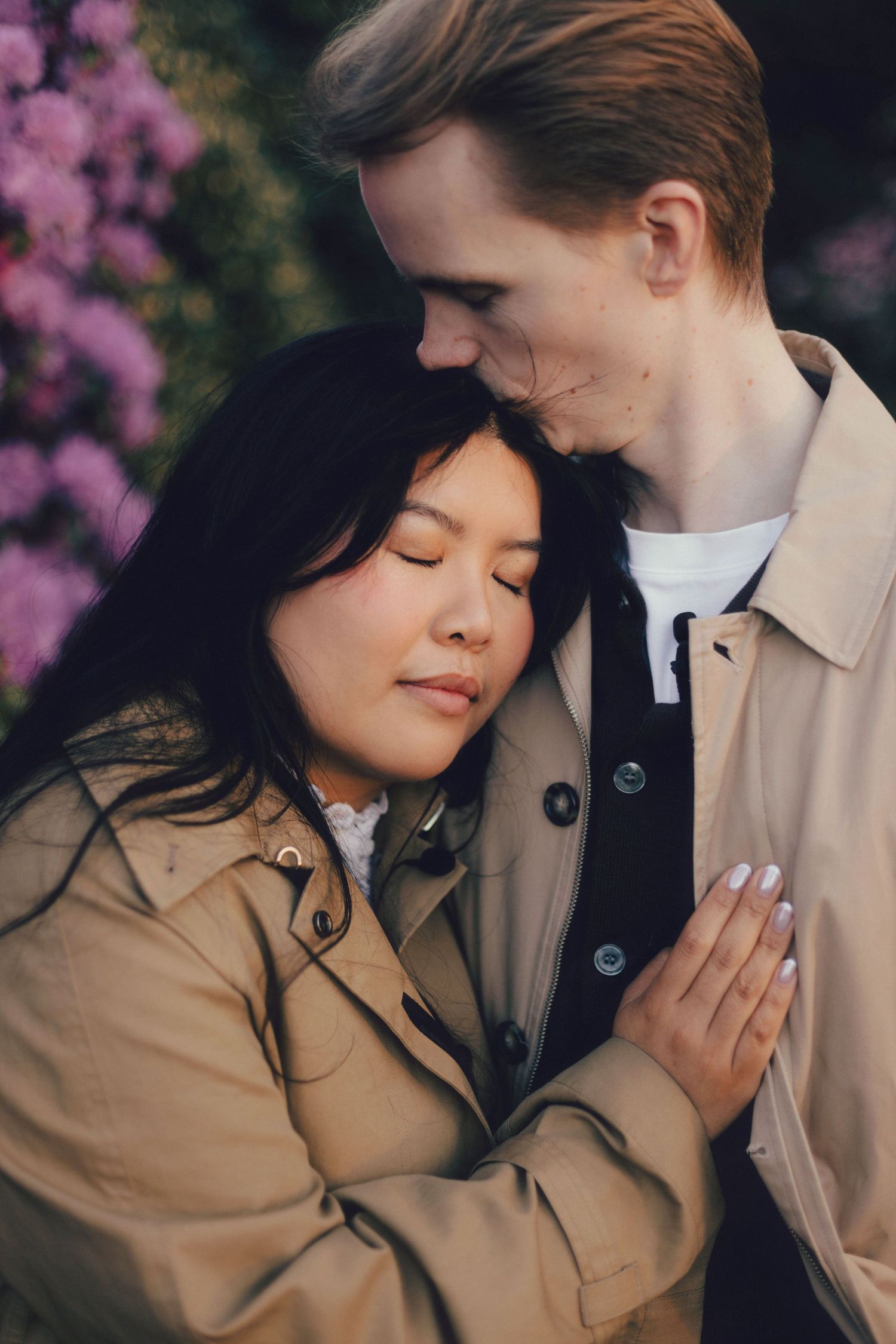 Romantic couple embraces tenderly against backdrop of pink cherry blossoms in spring garden.