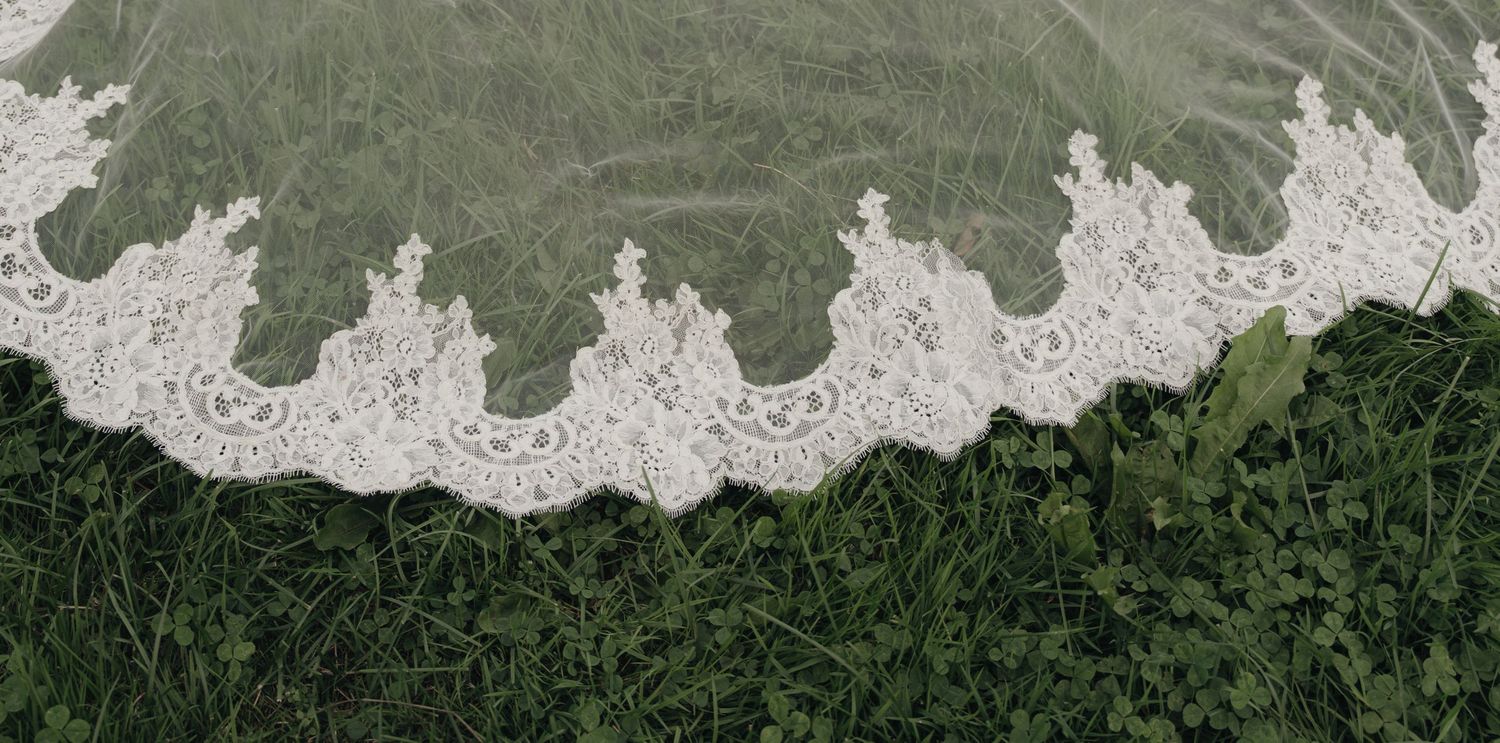 Sheer bridal veil with delicate scalloped ivory lace trim spread across green grass.