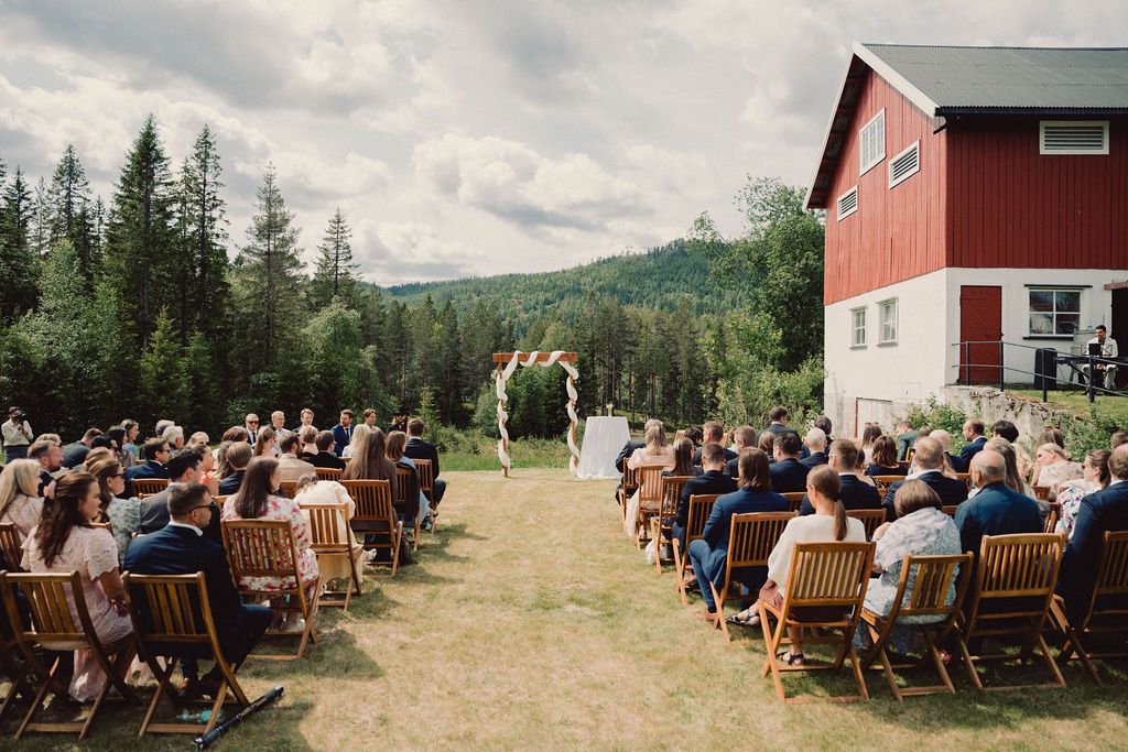 A panoramic view of an outdoor wedding ceremony with wooden chairs arranged in rows against a mountainous backdrop.