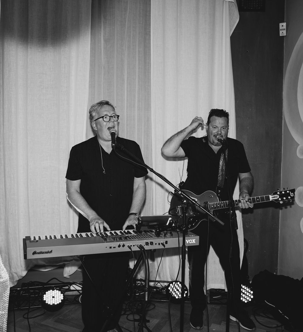 Black and white image of musicians performing on stage with instruments and electronic equipment.