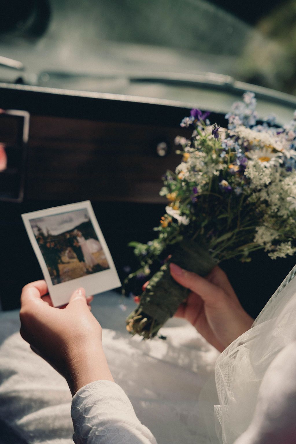 A person's hands hold vintage polaroid photos next to white flowers and delicate fabric in a wedding setting.