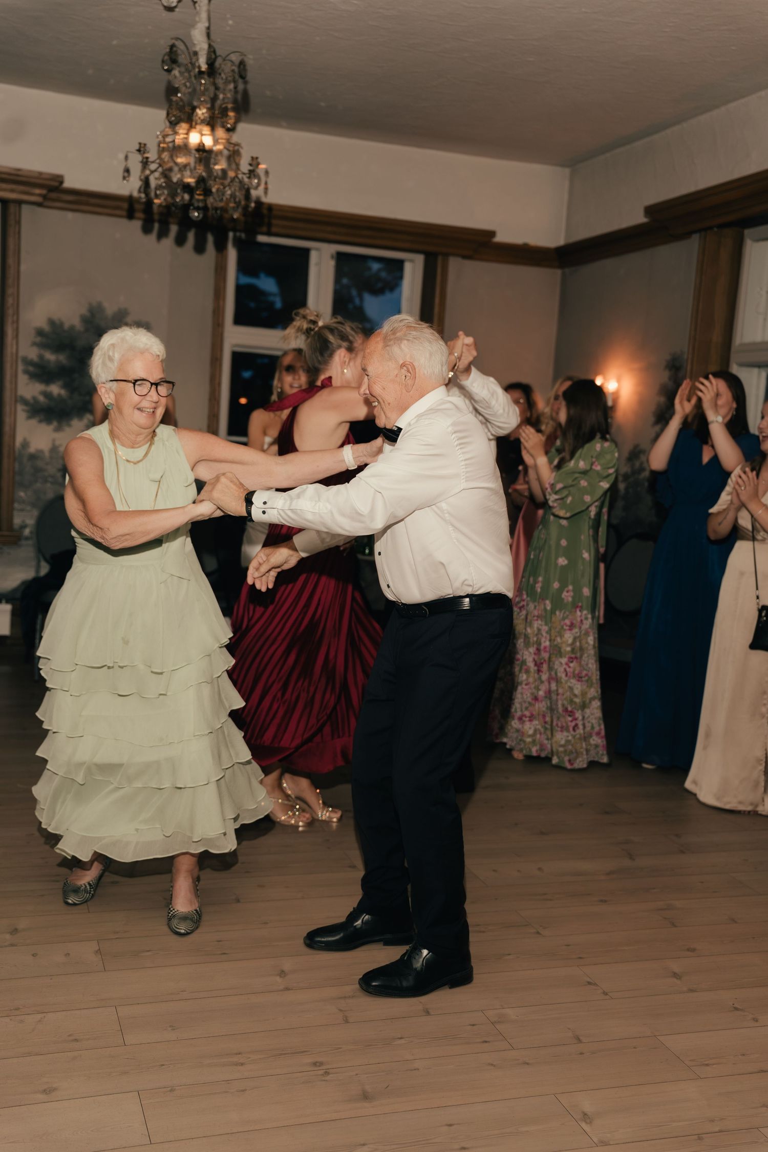 Elderly couple dancing joyfully at a wedding reception under a crystal chandelier.