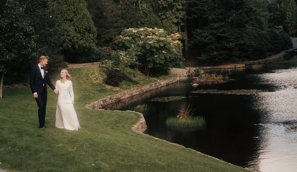 Bride and groom share a romantic moment by a serene pond in an elegant outdoor garden setting.