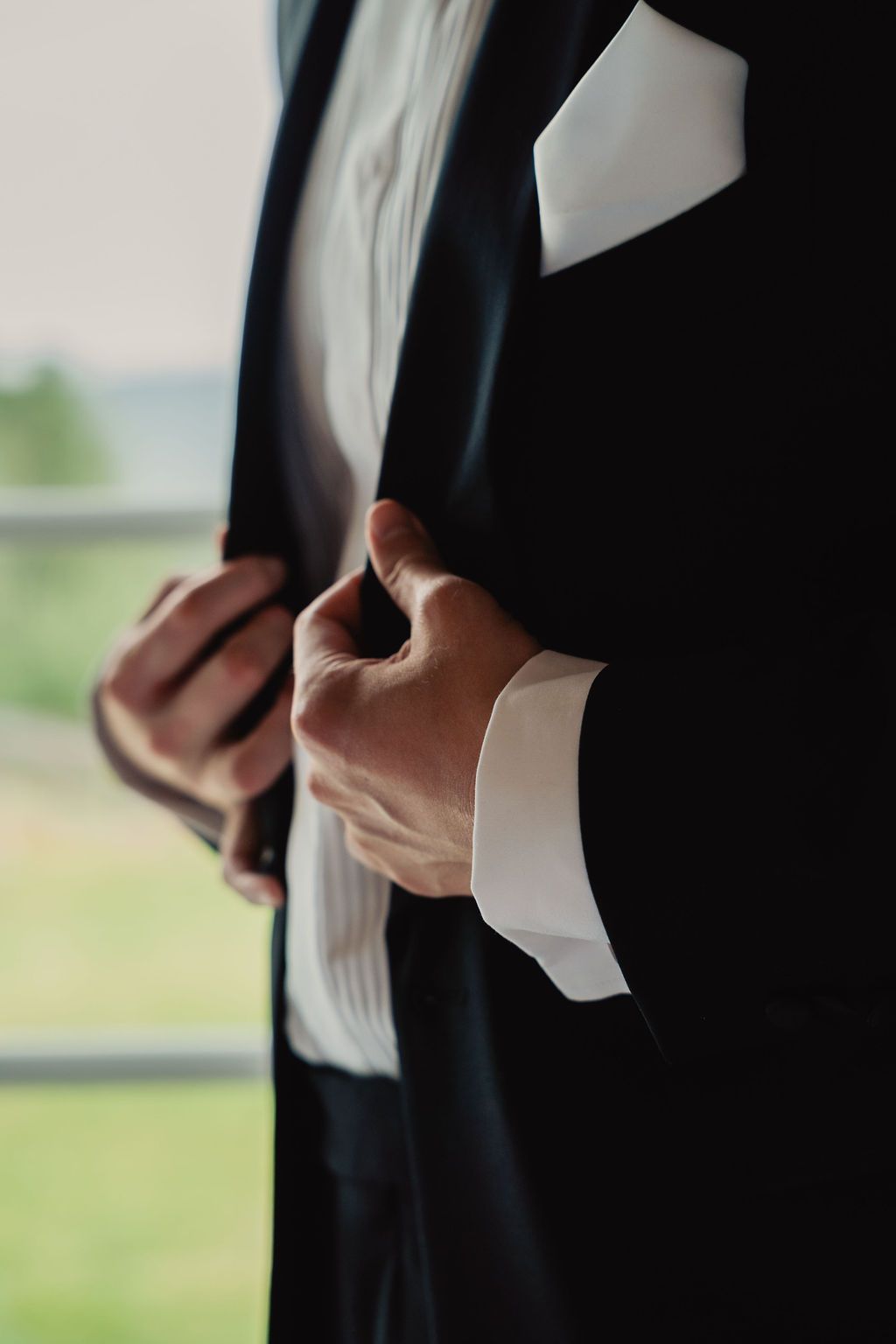 A close-up view of hands adjusting a black necktie against a white shirt with blurred background.