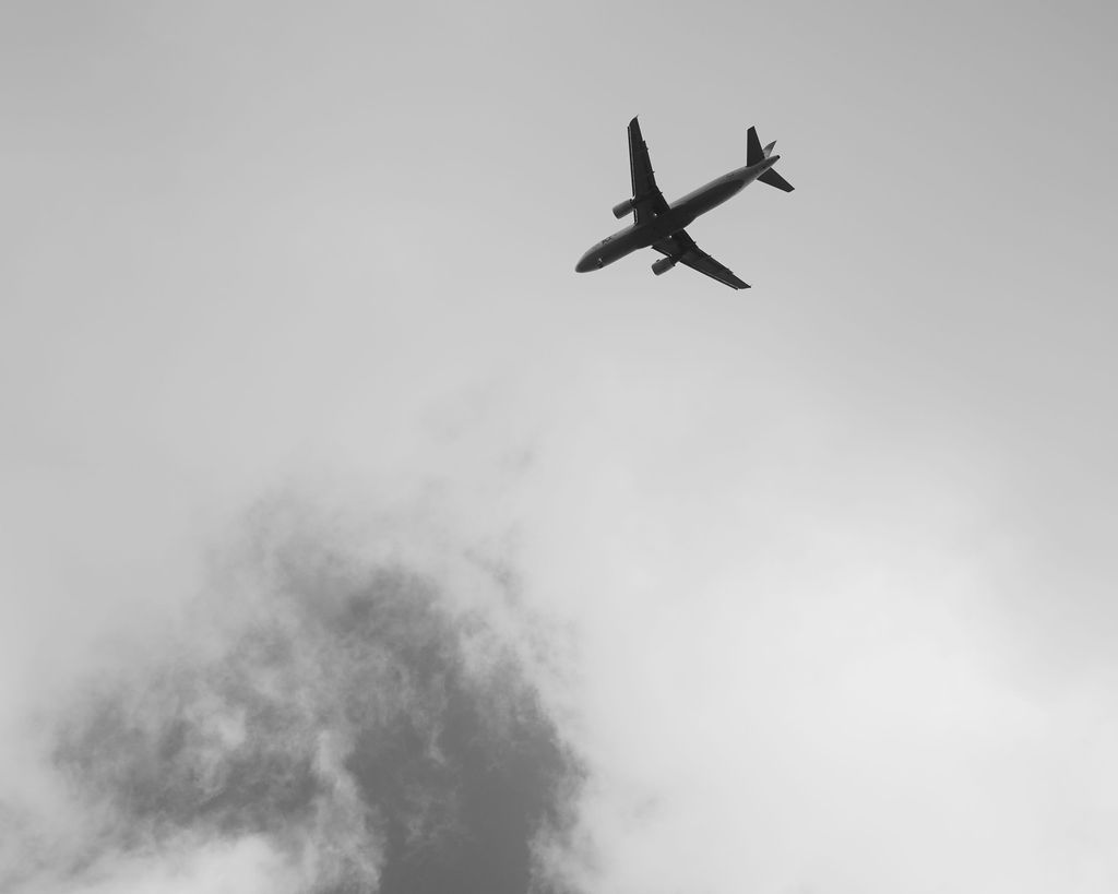 A silhouette of a commercial airplane flying through cloudy skies against a dramatic gray background.