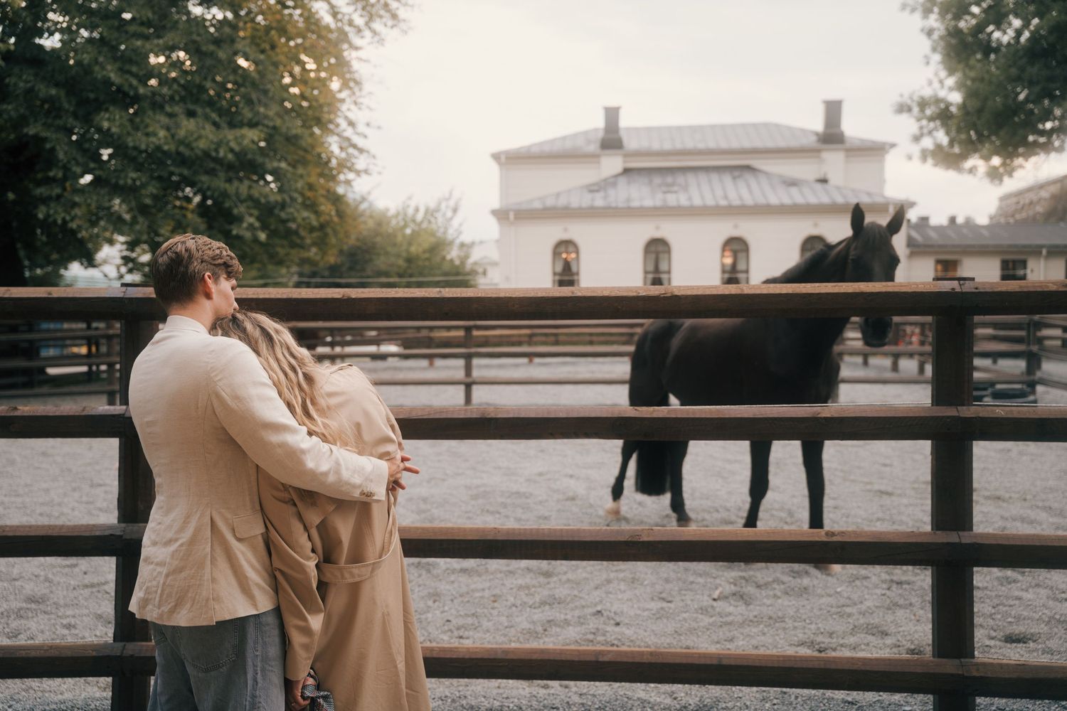 A couple embraces near a rustic wooden fence at sunset, creating a romantic silhouette against the golden light.