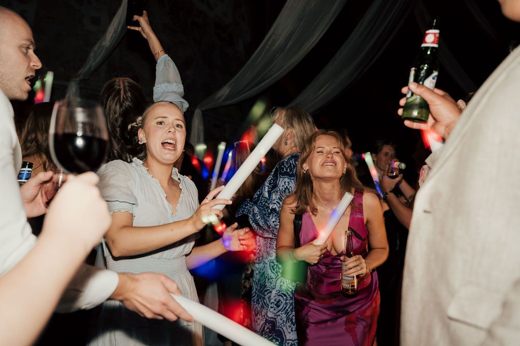 People dancing and celebrating at a wedding reception with colorful lighting and festive atmosphere.