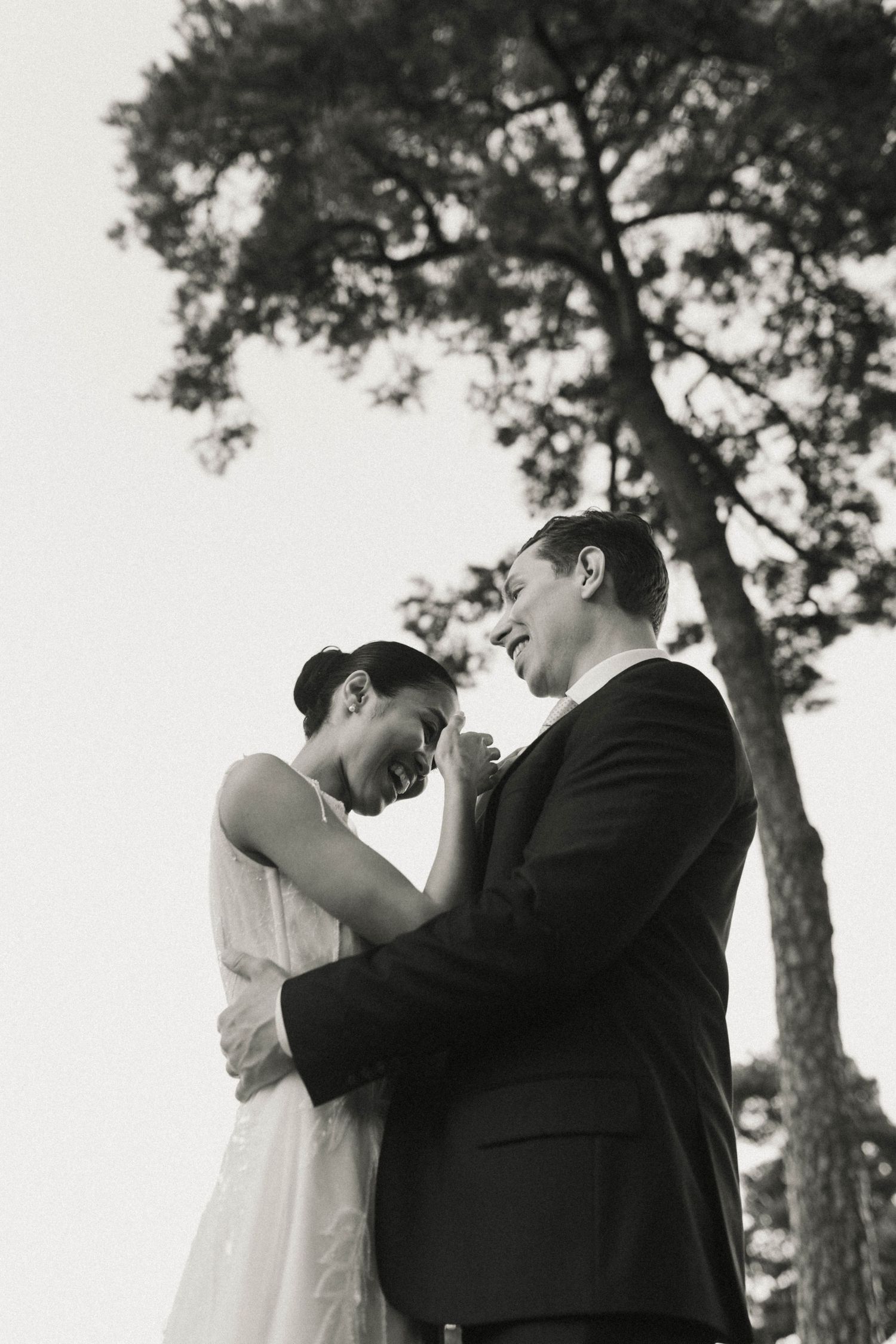 Three black and white romantic wedding photos show intimate moments between couples embracing under tall pine trees.