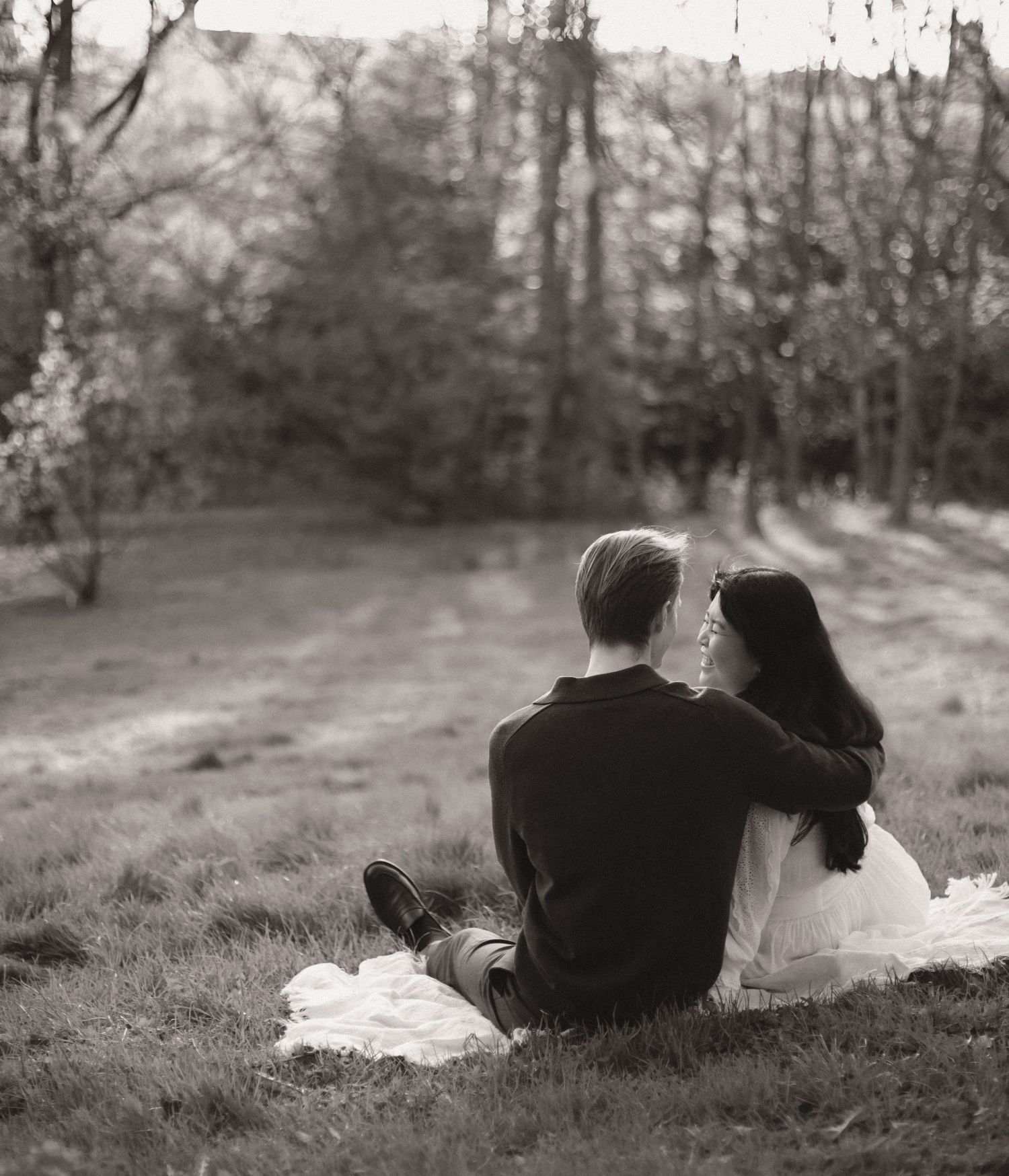 Black and white photo of two people lying on a grassy hillside in a tranquil wooded setting.